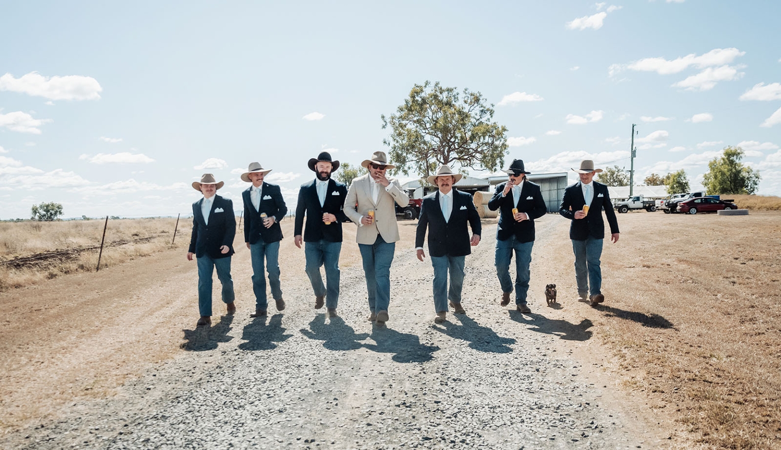 capella wedding photography – caitlin & adam’s farm wedding 120 Seven groomsmen in blazers, jeans and cowboy hats walking along a gravel road at a Capella farm wedding