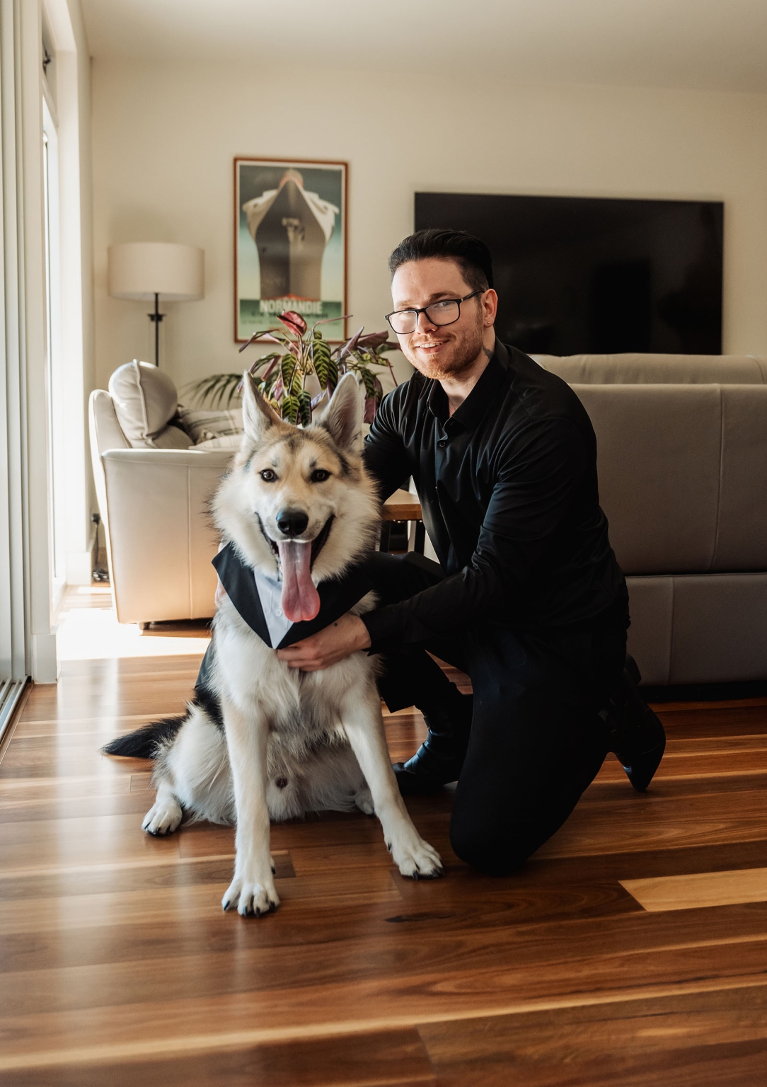 kuitpo hall wedding - courtney & jarrod 191 Man posing with tuxedo-clad husky dog in a modern living room.