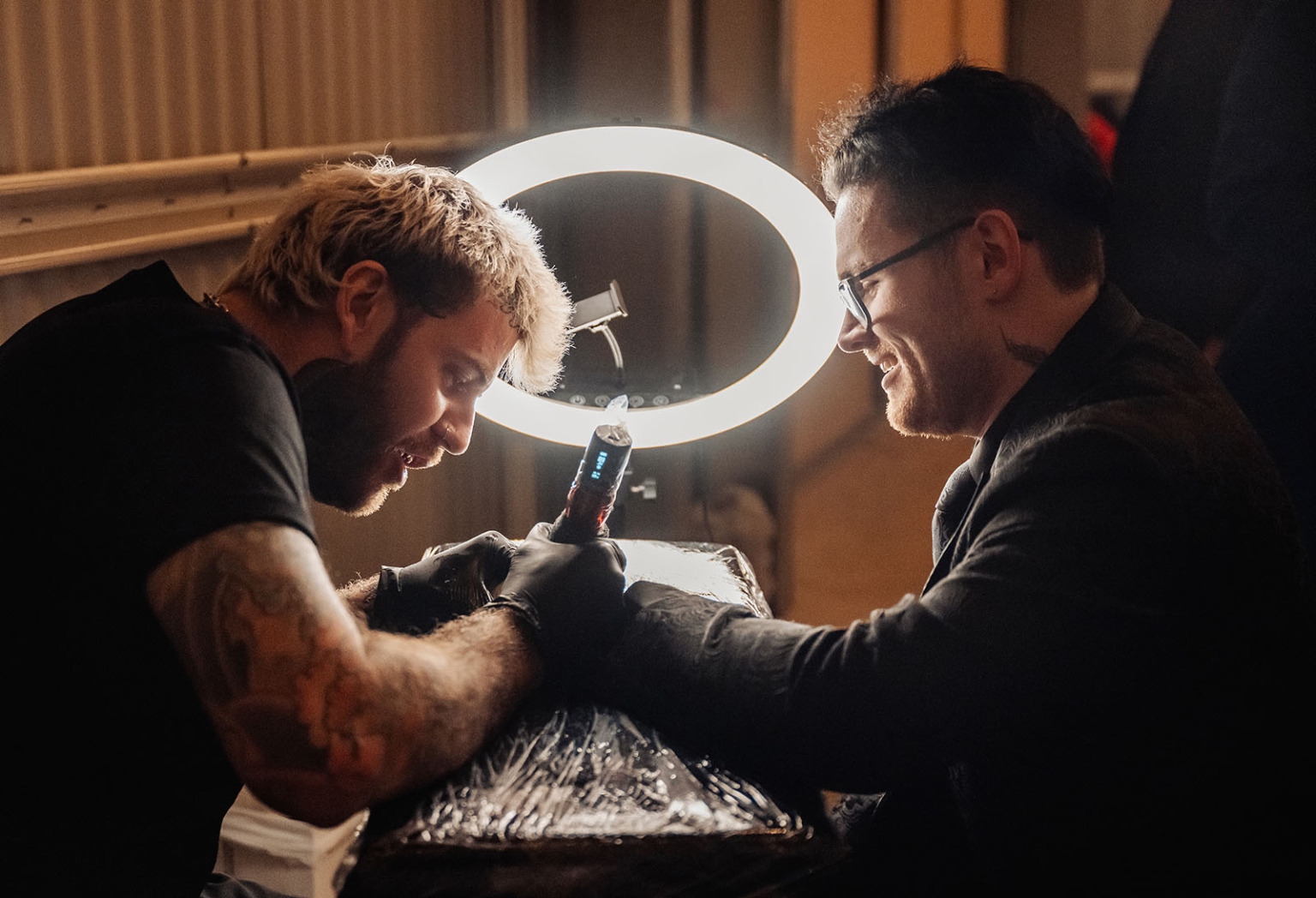 kuitpo hall wedding - courtney & jarrod 262 Tattoo artist works on client under ring light in professional studio.