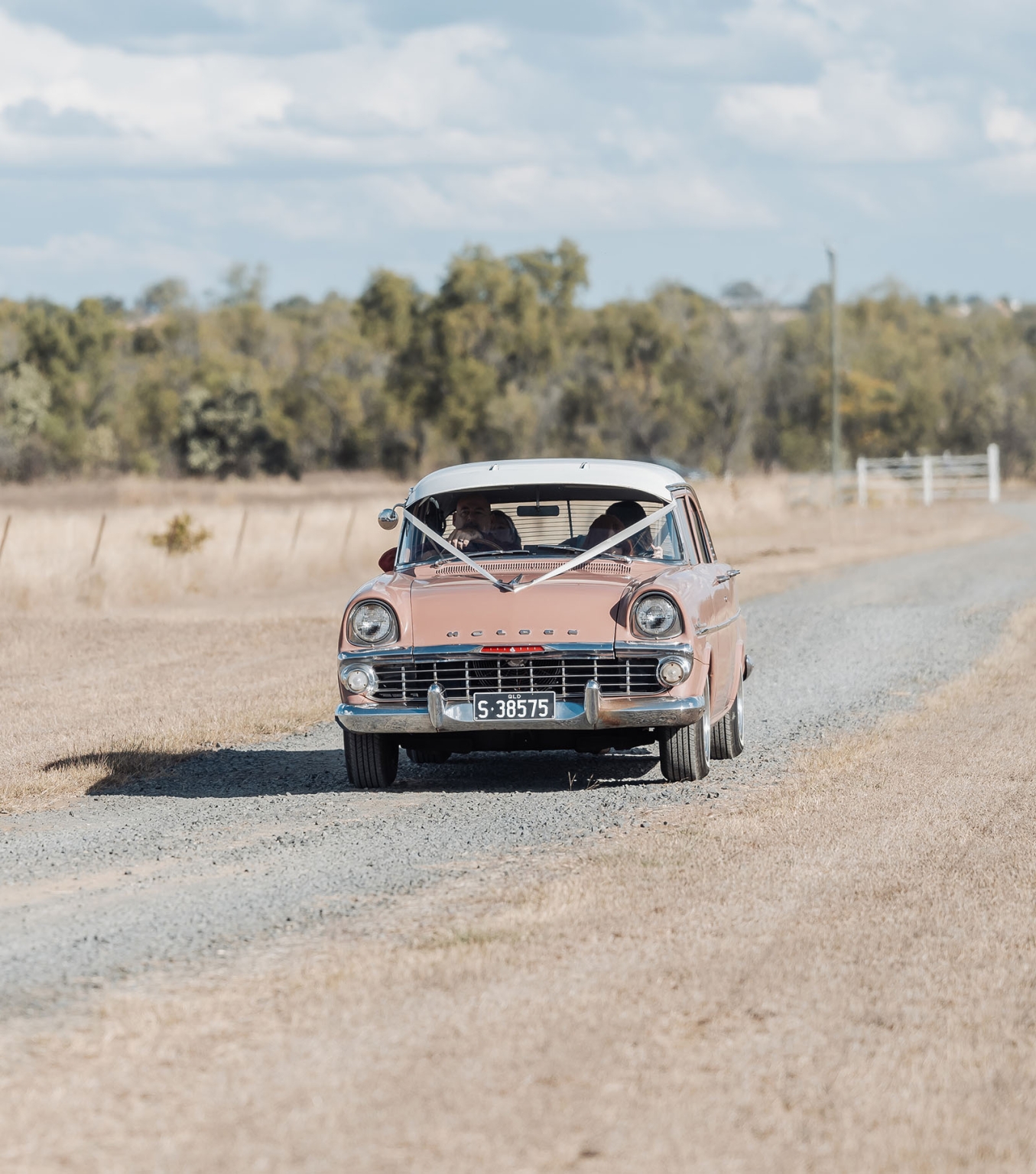capella wedding photography – caitlin & adam’s farm wedding 137 Vintage pink wedding car decorated with white ribbons driving along a gravel farm road in Capella