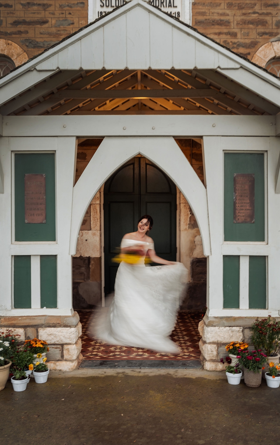 keyneton soldier's memorial hall wedding - lara & simon 31 Bride in an off-the-shoulder white wedding dress twirling with a yellow bouquet in the entrance of Keyneton church