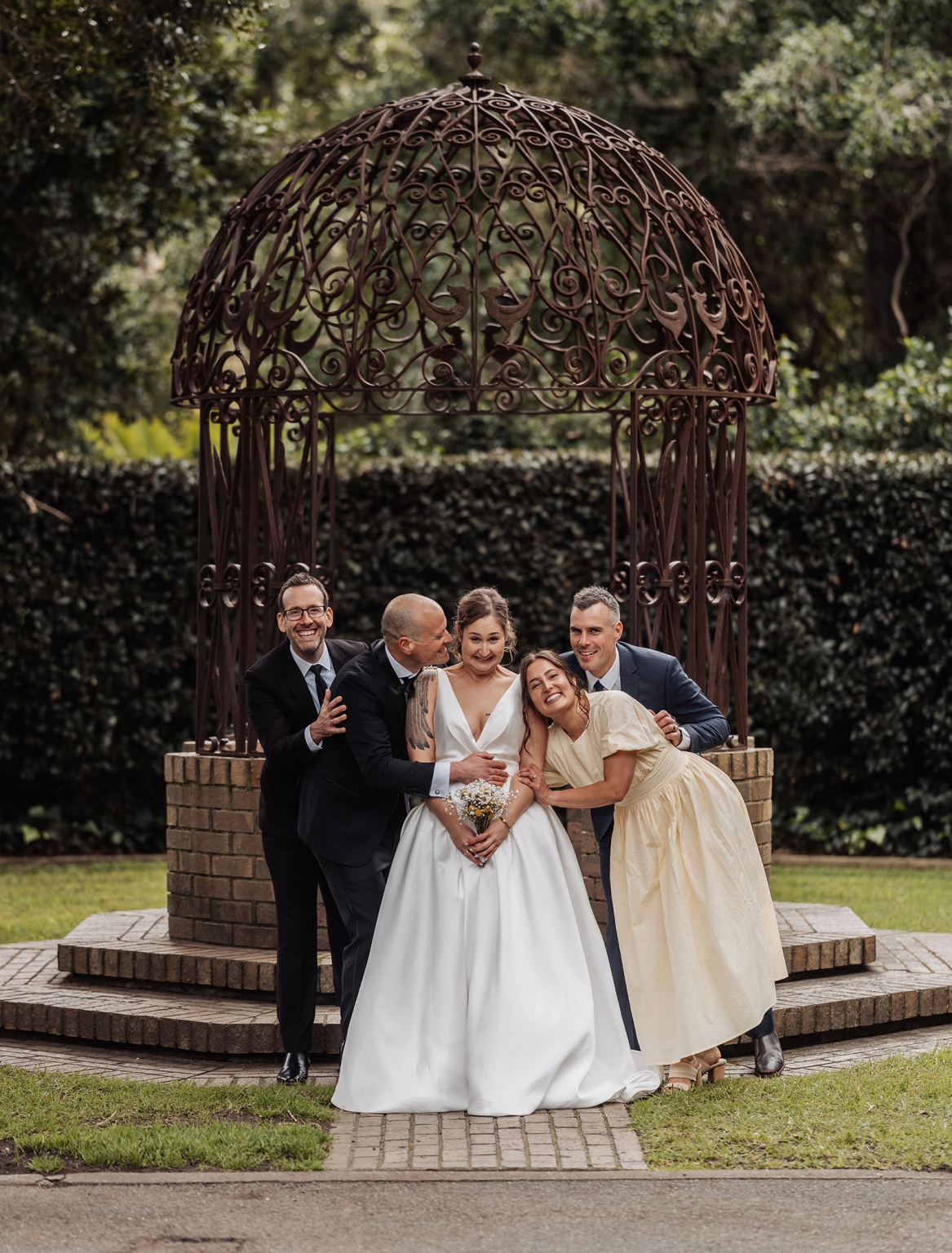 marriage registration office wedding - mia & roberto 75 Bride in a white gown laughing with her wedding party beneath an ornate iron gazebo in a leafy garden