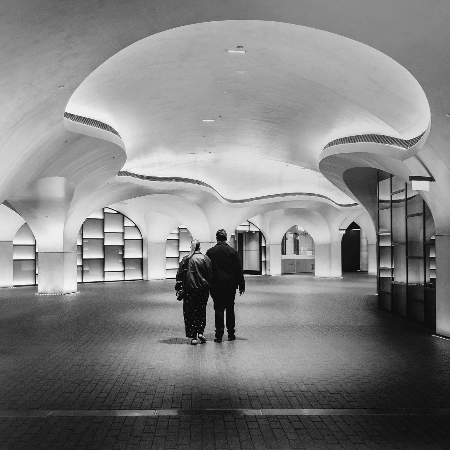 elder park rotunda proposal - lauren & enrique 16 Lauren and Enrique walking through a softly lit interior with sweeping curved arches