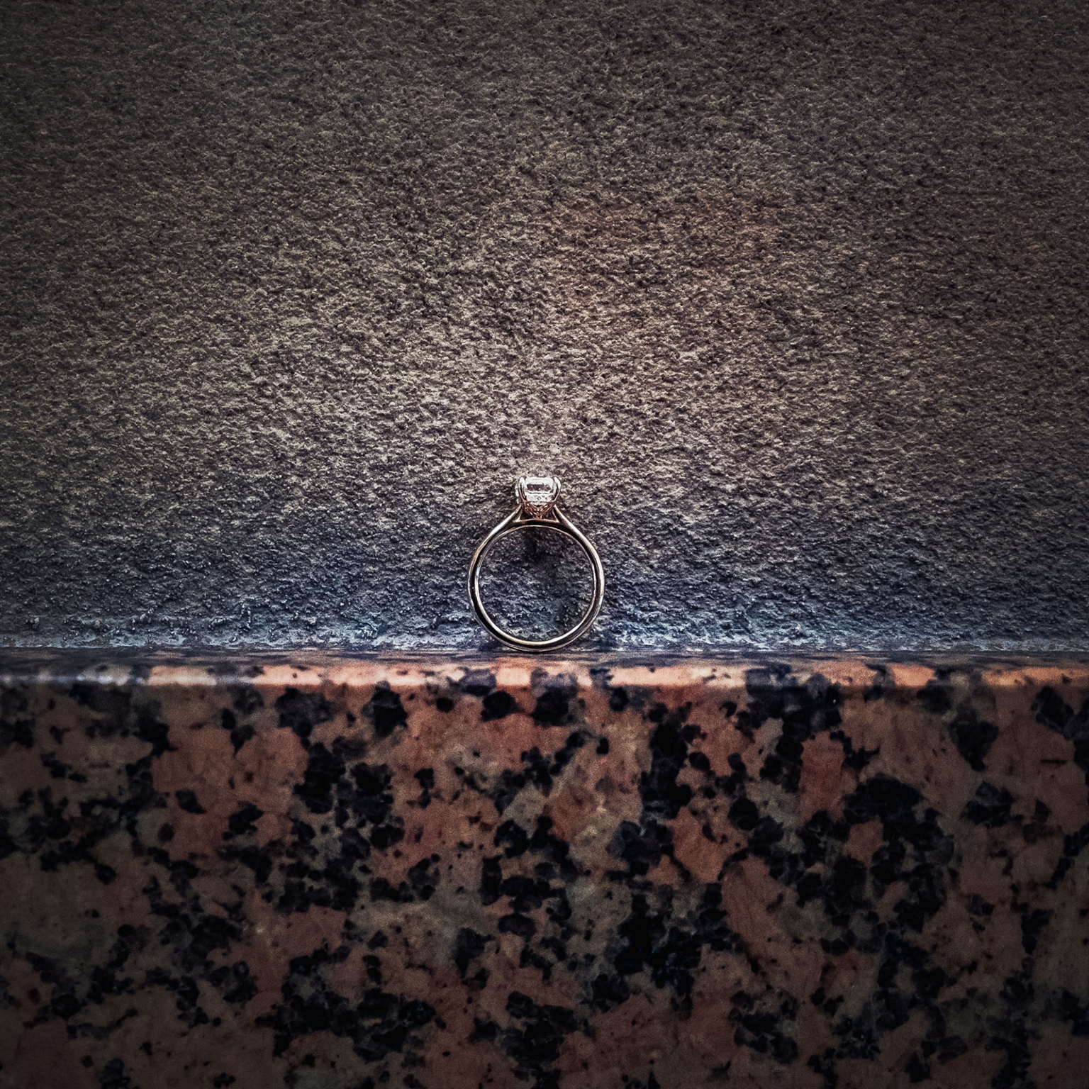 elder park rotunda proposal - lauren & enrique 19 Solitaire engagement ring resting against a textured stone ledge at Elder Park