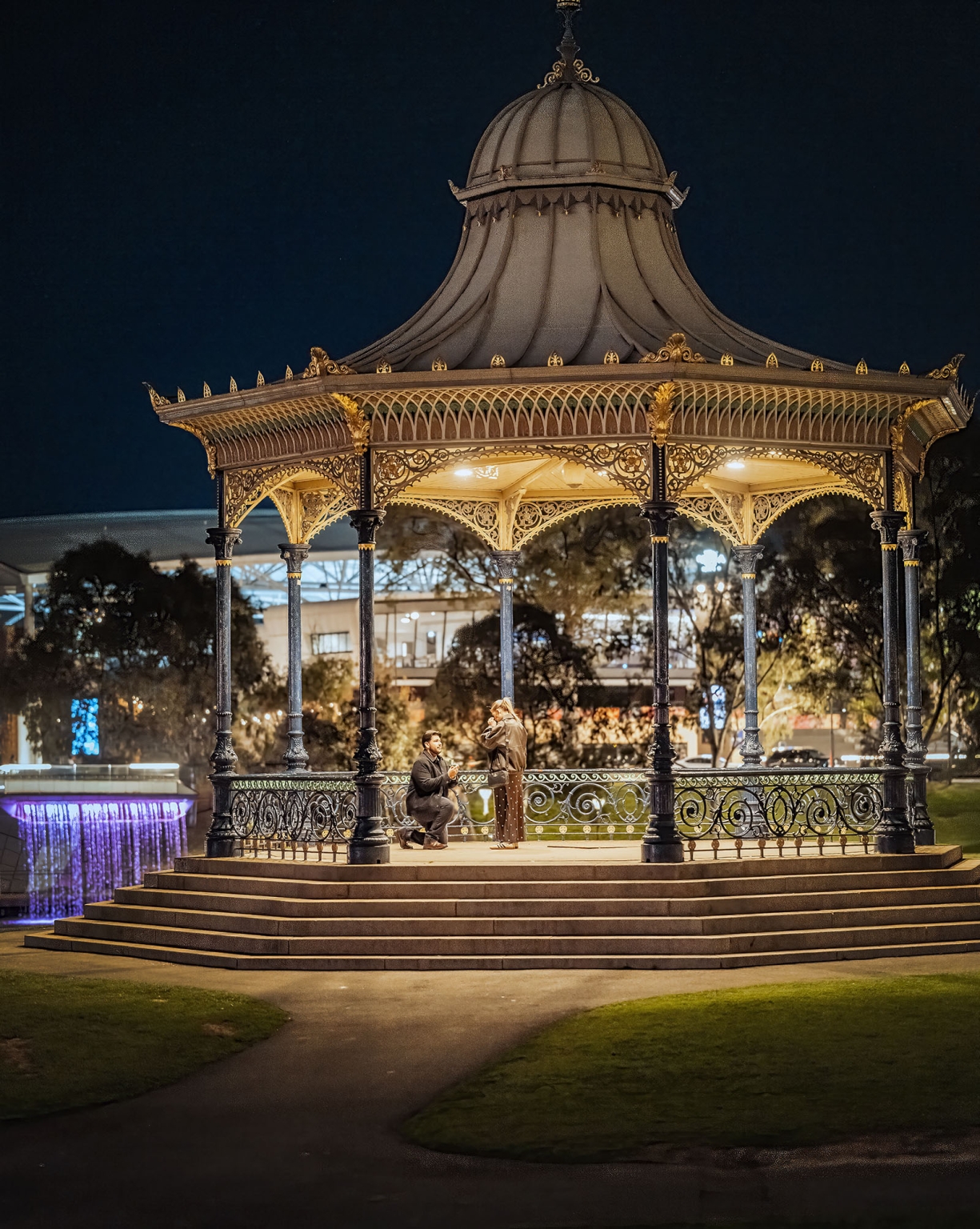 elder park rotunda proposal - lauren & enrique 1 Enrique kneeling to propose to Lauren beneath the illuminated Elder Park Rotunda at night