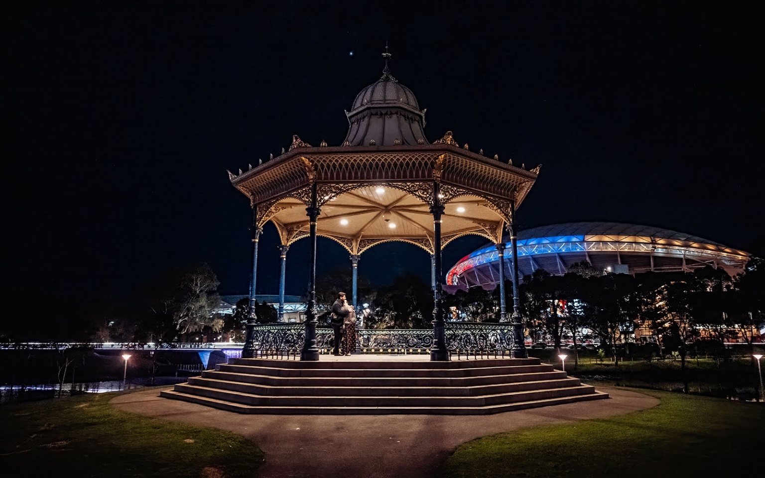 elder park rotunda proposal - lauren & enrique 3 Lauren and Enrique embracing beneath the illuminated Elder Park Rotunda at night in Adelaide