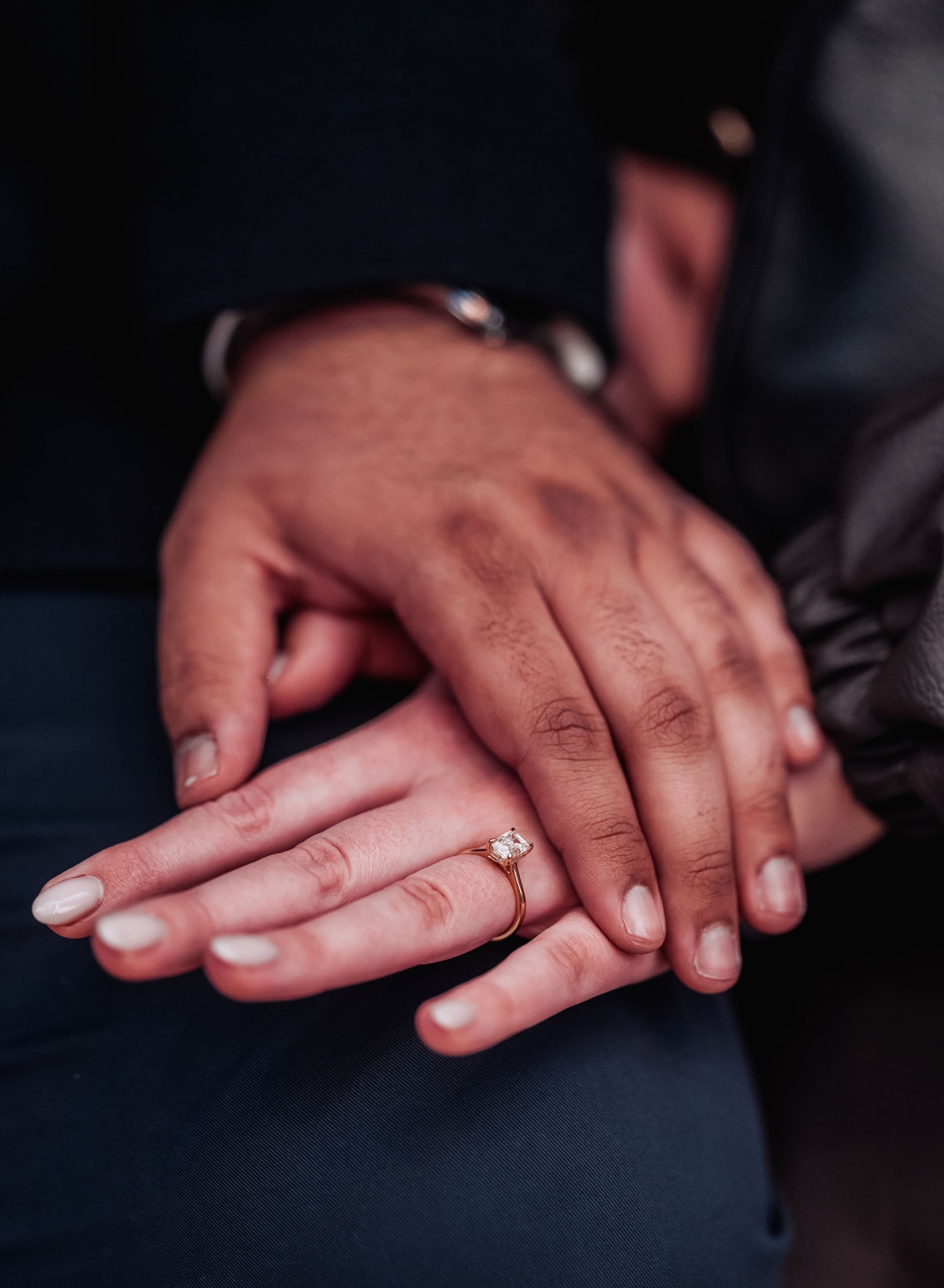 elder park rotunda proposal - lauren & enrique 22 Close-up of two hands resting together, showing a gold engagement ring with a square-cut diamond.