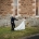 Lara and Simon holding hands outside the stone Keyneton church, with Lara carrying a colourful bouquet.