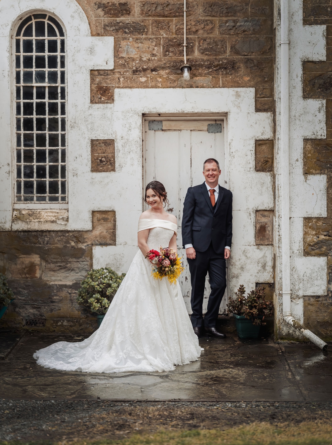 keyneton soldier's memorial hall wedding - lara & simon 25 Lara and Simon standing outside Keyneton Church, with Lara holding a colourful bouquet in her off-the-shoulder wedding gown