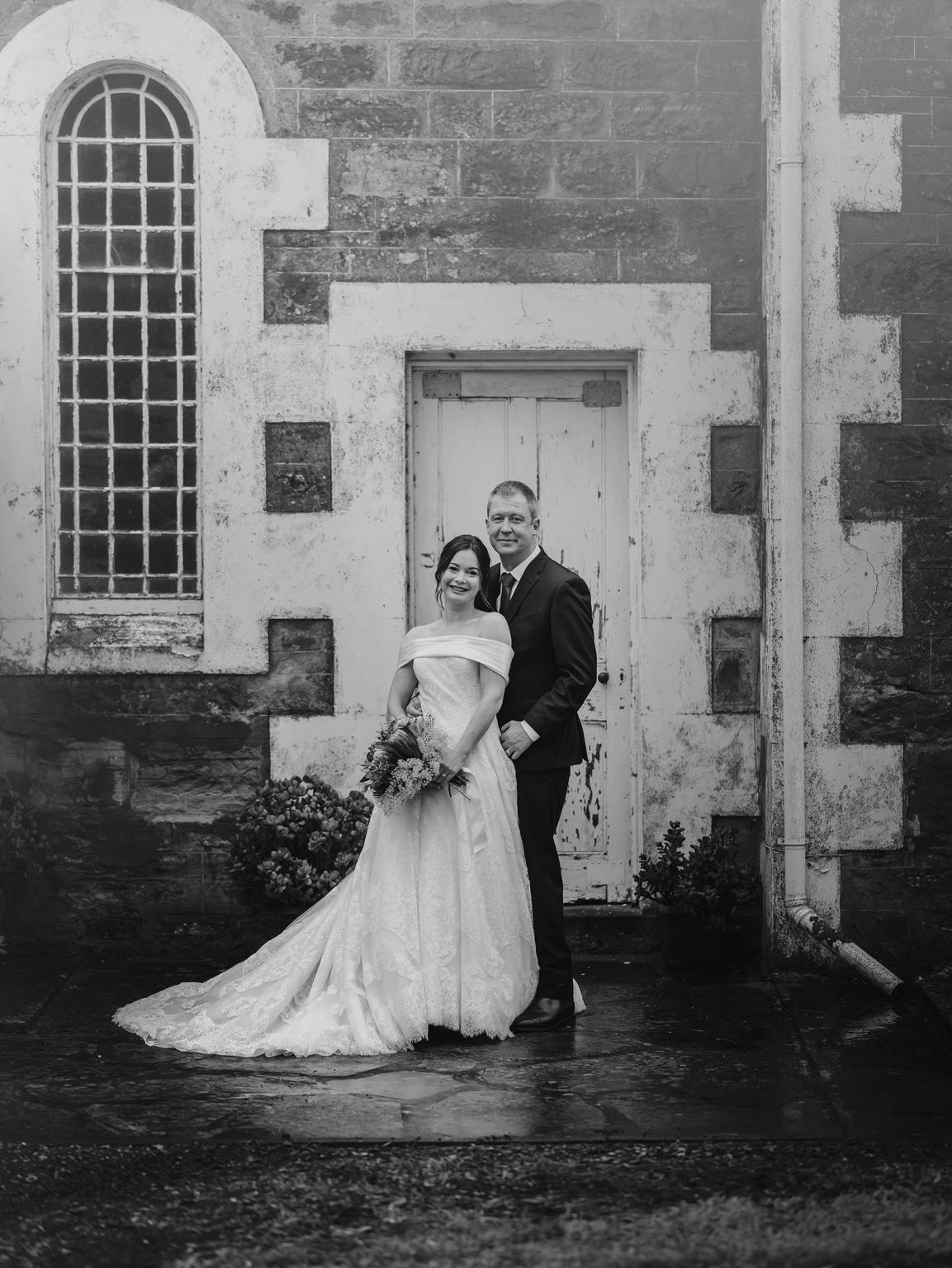 keyneton soldier's memorial hall wedding - lara & simon 26 Lara and Simon standing outside the weathered stone entrance of Keyneton Church, with Lara holding her bouquet.