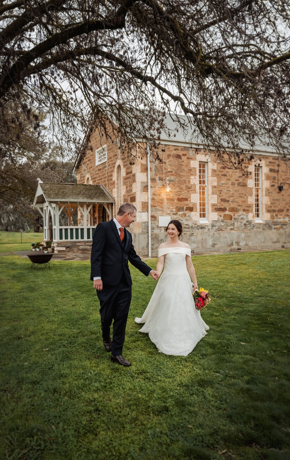 keyneton soldier's memorial hall wedding - lara & simon 35 Lara and Simon holding hands on the lawn outside Keyneton Church, with the stone church building behind them