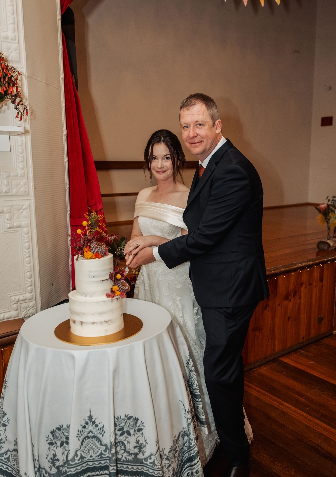 keyneton soldier's memorial hall wedding - lara & simon 45 Lara and Simon cutting their two-tier wedding cake decorated with red, orange and yellow flowers at Keyneton Soldier's Memorial Hall