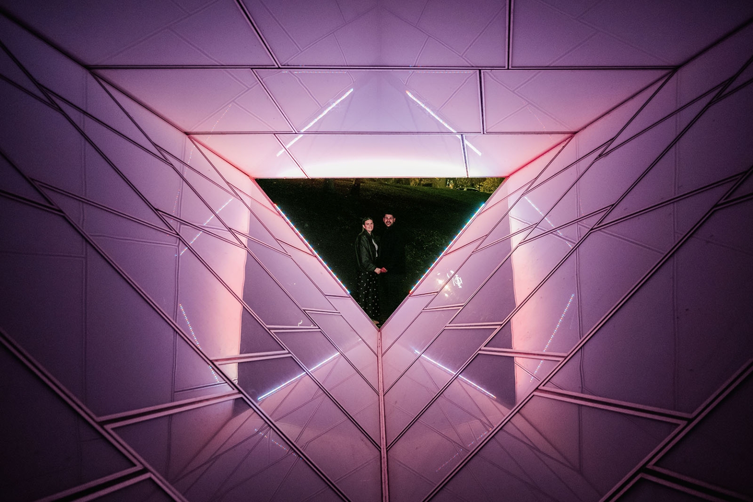 elder park rotunda proposal - lauren & enrique 14 Lauren and Enrique standing together beyond a triangular opening in a pink-lit geometric installation
