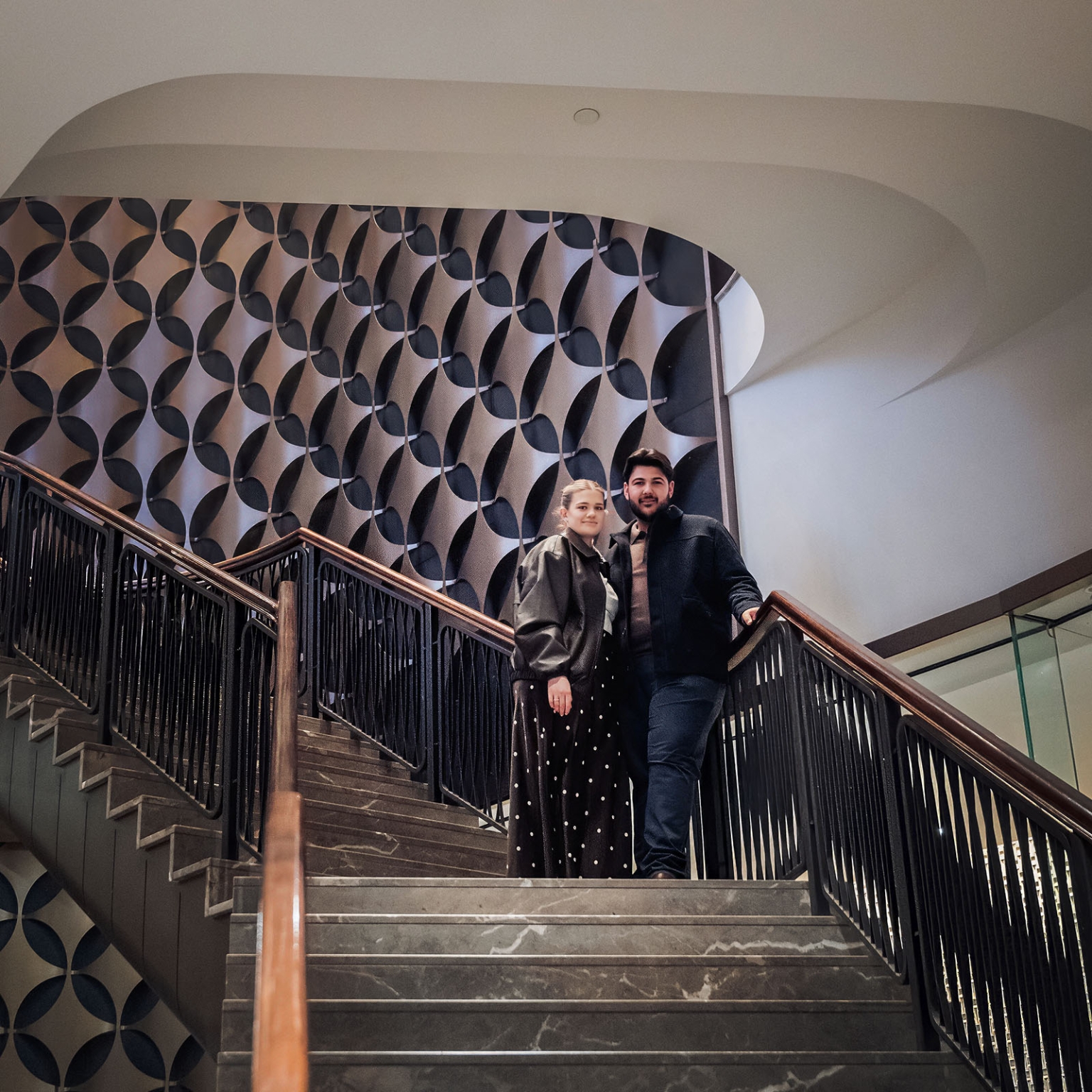 elder park rotunda proposal - lauren & enrique 21 Lauren and Enrique standing together on an indoor staircase with black railings and patterned wall panels