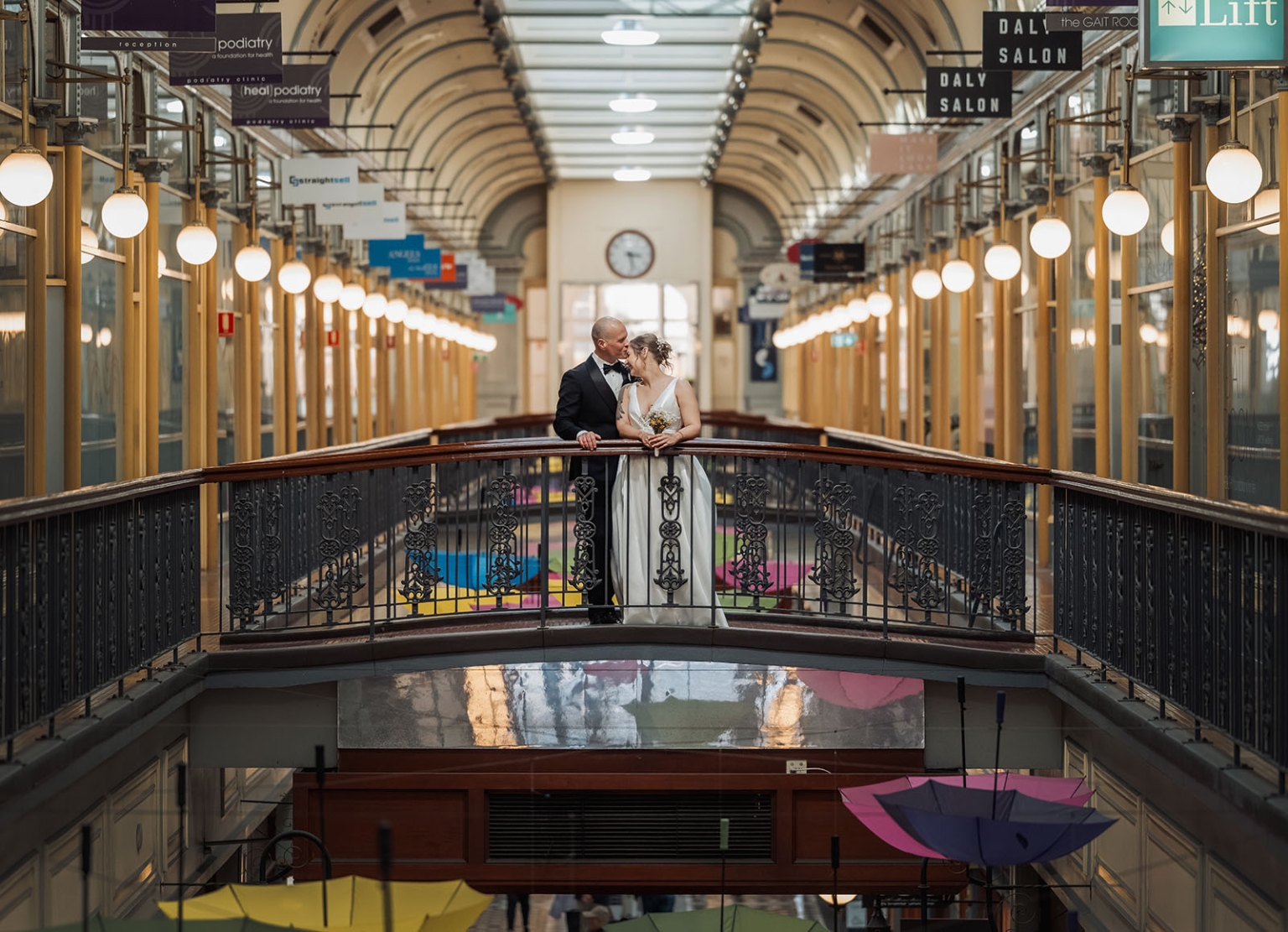 marriage registration office wedding - mia & roberto 100 Mia and Roberto kissing on an ornate bridge inside Adelaide Arcade, with glowing globe lights and shopfronts behind them.