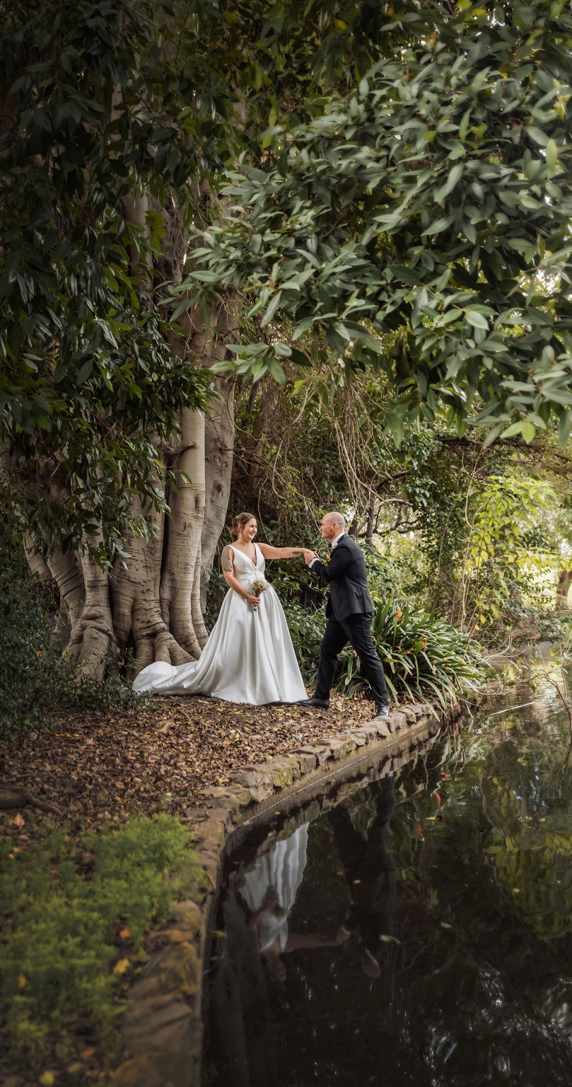 marriage registration office wedding - mia & roberto 84 Mia and Roberto holding hands beside a pond beneath a large fig tree in Adelaide Botanic Park