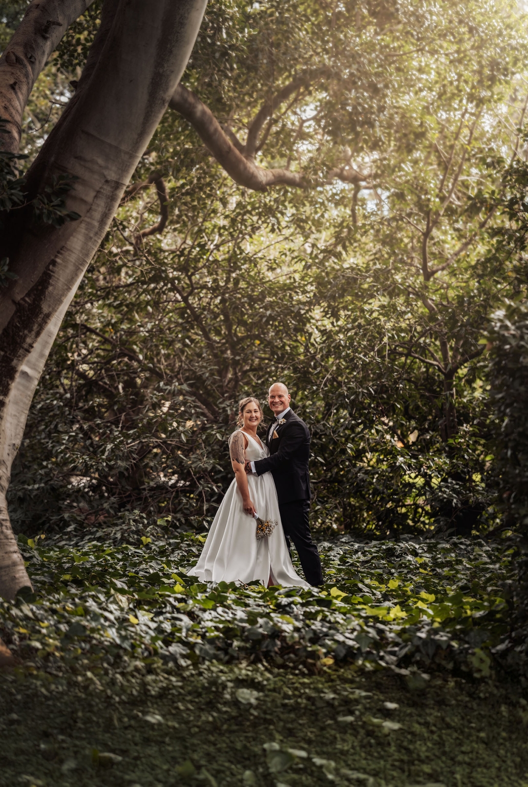 marriage registration office wedding - mia & roberto 74 Mia and Roberto in wedding attire standing beneath a large fig tree in Adelaide Botanic Park