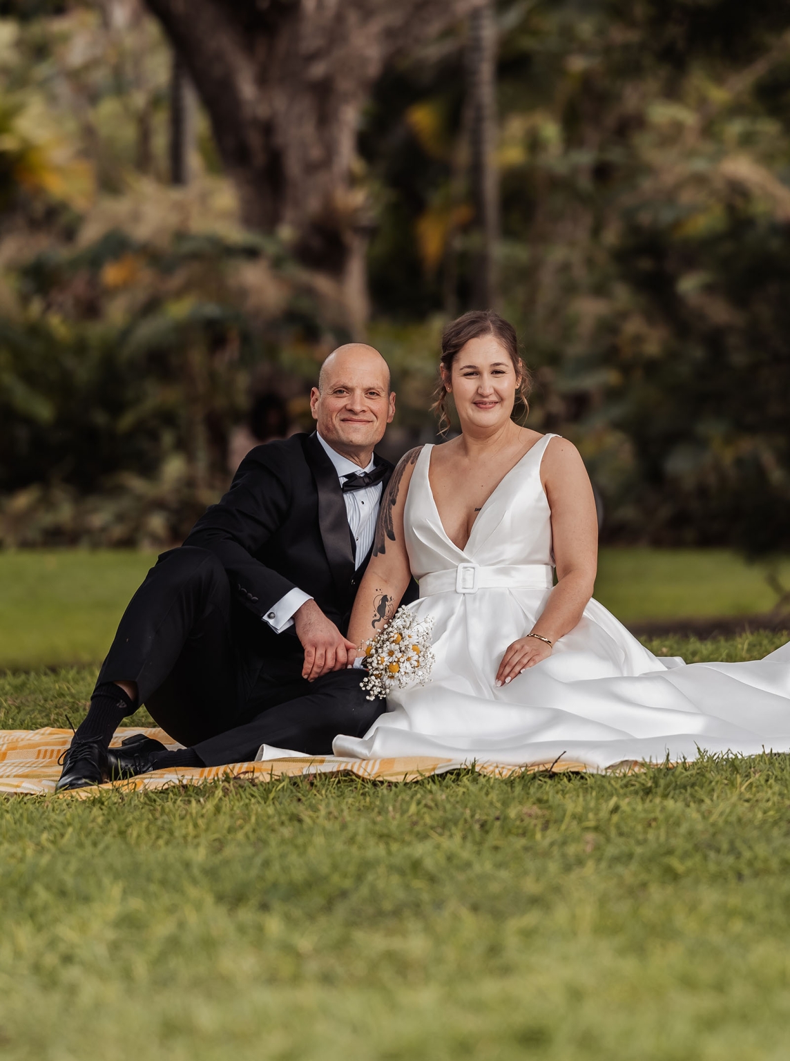 marriage registration office wedding - mia & roberto 78 Mia and Roberto seated together on a picnic blanket in Adelaide Botanic Park, wearing wedding attire.