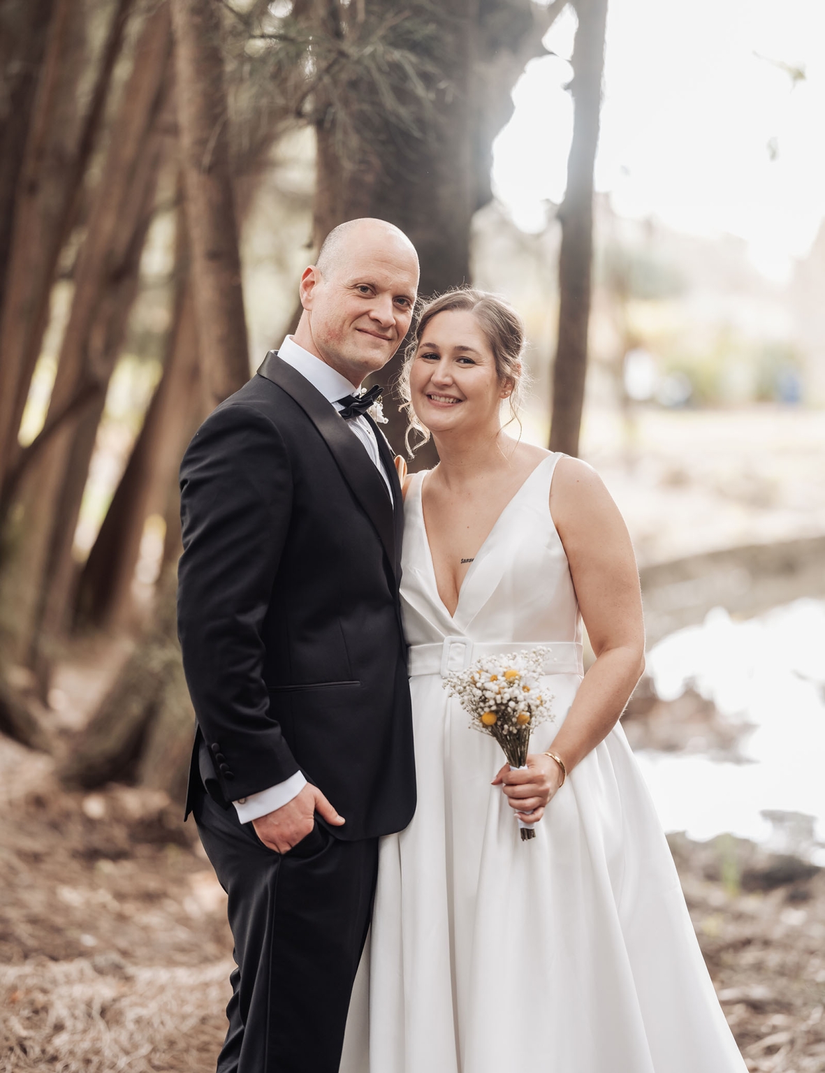 marriage registration office wedding - mia & roberto 80 Mia and Roberto smiling together beneath large fig trees at Adelaide Botanic Park, with Mia holding a small yellow and white bouquet.