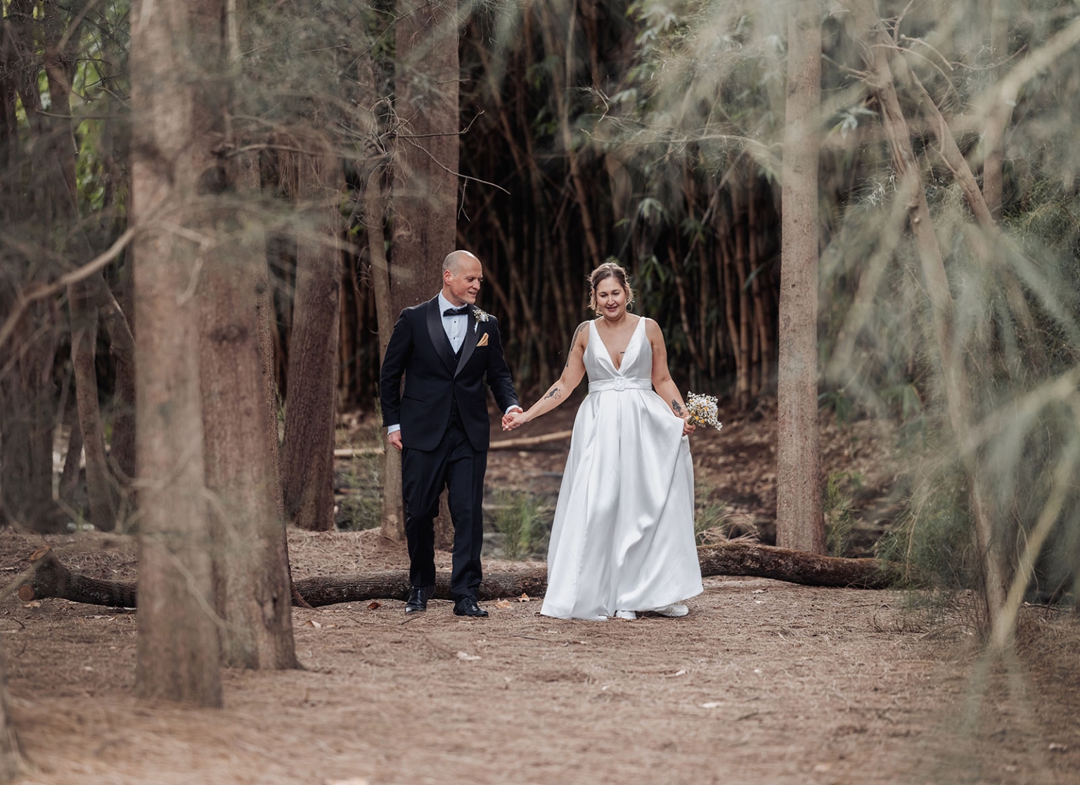 marriage registration office wedding - mia & roberto 81 Mia and Roberto walk hand in hand through trees in Botanic Park, with Mia in a white wedding dress and Roberto in a black tuxedo.