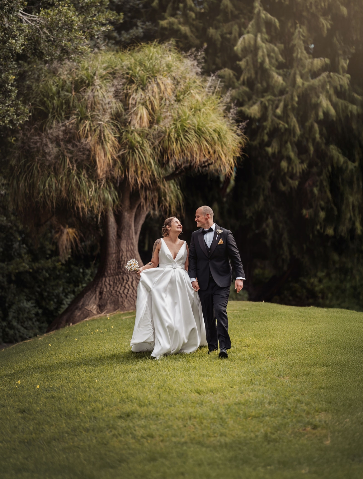 marriage registration office wedding - mia & roberto 72 Mia and Roberto walking hand in hand across a lawn in wedding attire beneath leafy trees in Adelaide Botanic Park.