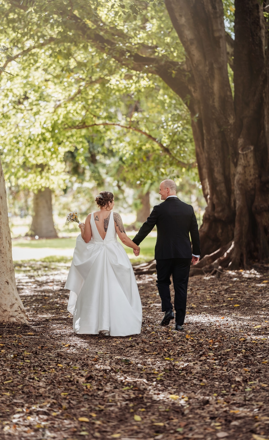 marriage registration office wedding - mia & roberto 55 Mia and Roberto holding hands as they walk beneath large trees in Adelaide Botanic Park