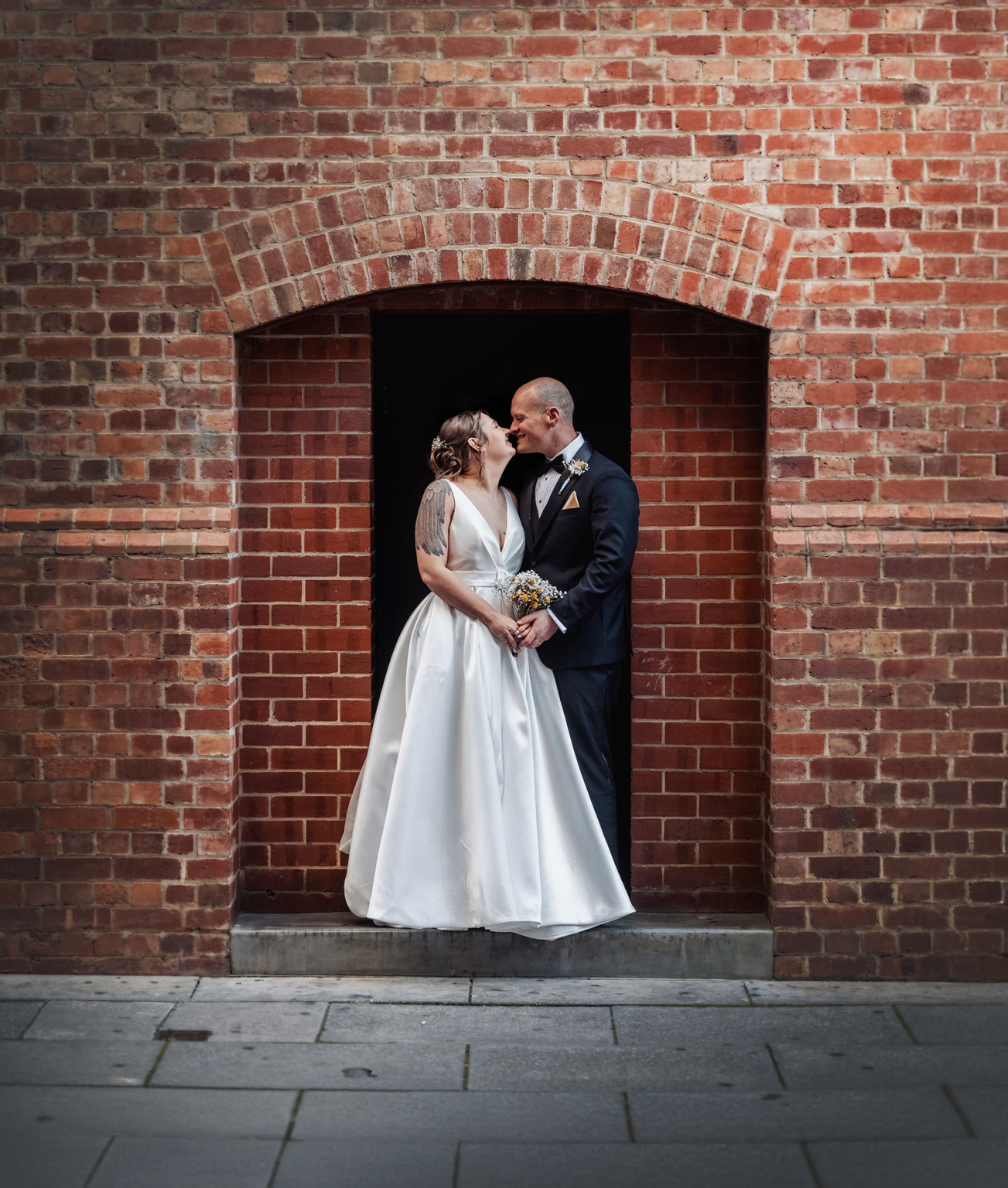 marriage registration office wedding - mia & roberto 95 Mia and Roberto standing together beneath a red brick archway, wearing a white wedding dress and dark suit