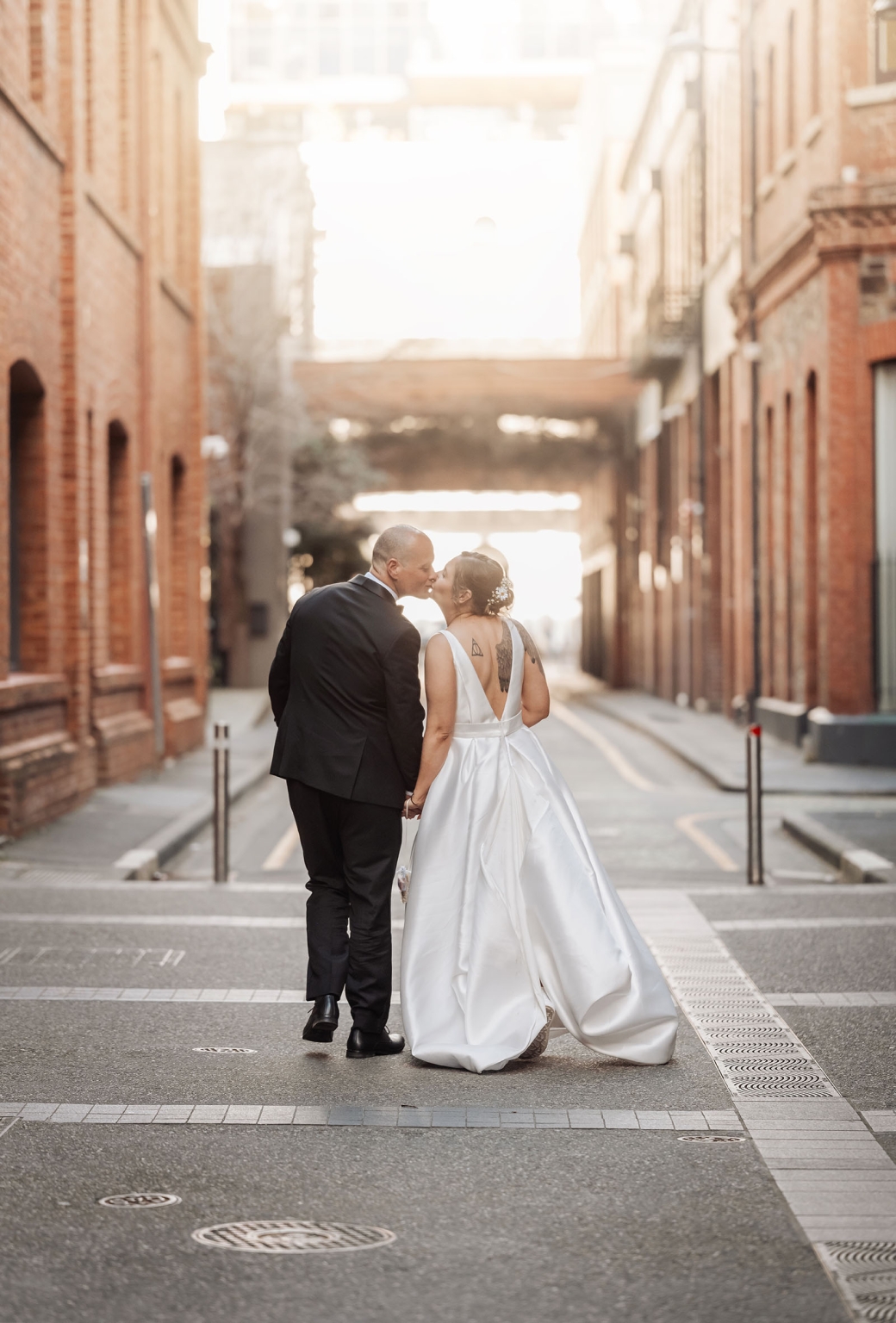 marriage registration office wedding - mia & roberto 92 Mia and Roberto holding hands and kissing in a sunlit city laneway after their wedding