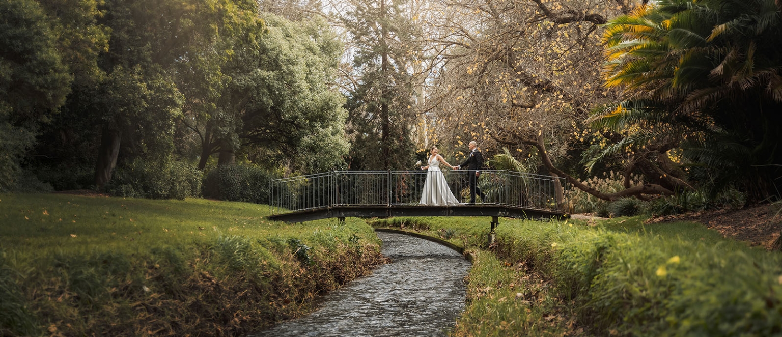 marriage registration office wedding - mia & roberto 66 Mia and Roberto holding hands on a small footbridge above a creek, surrounded by lush garden foliage