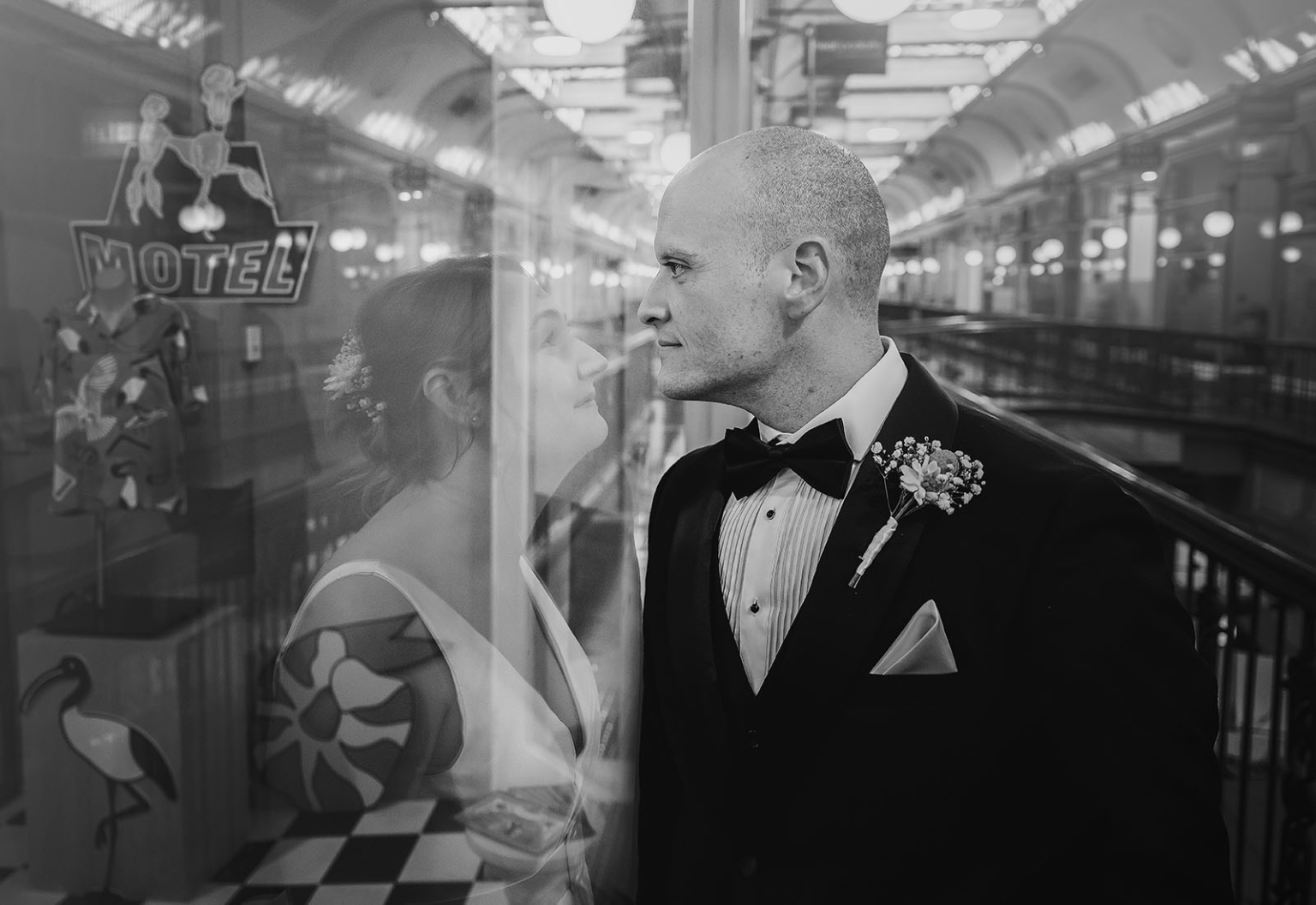 marriage registration office wedding - mia & roberto 102 Mia and Roberto facing one another through a glass reflection in a motel corridor, with Roberto wearing a black tuxedo and Mia in a white wedding dress.