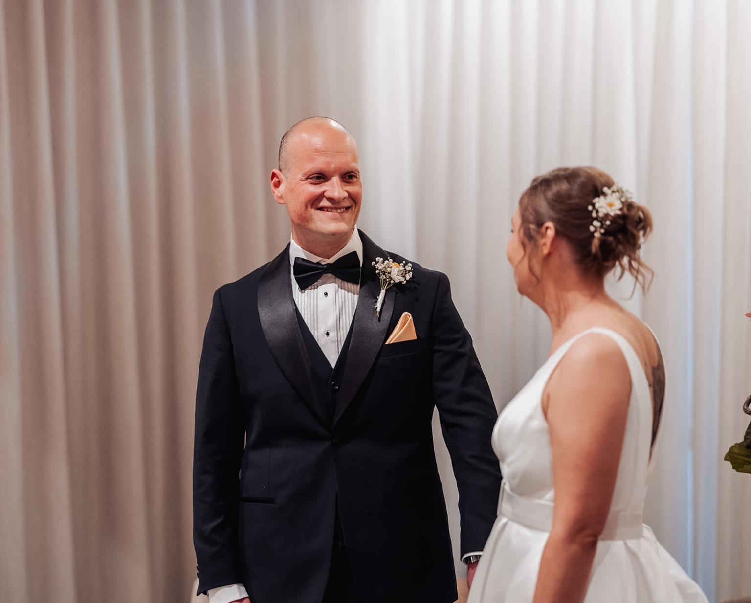 marriage registration office wedding - mia & roberto 86 Roberto in a black tuxedo smiling at Mia in her white wedding dress before pale draped curtains