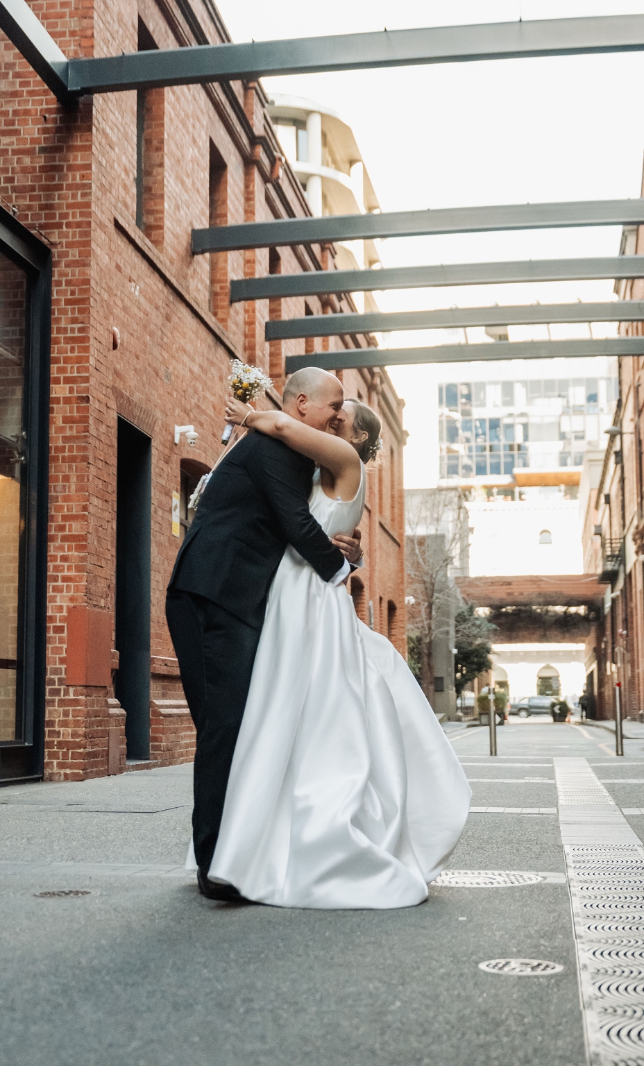 marriage registration office wedding - mia & roberto 93 Mia and Roberto embracing in a city laneway, with Mia holding a small bouquet in her white wedding dress