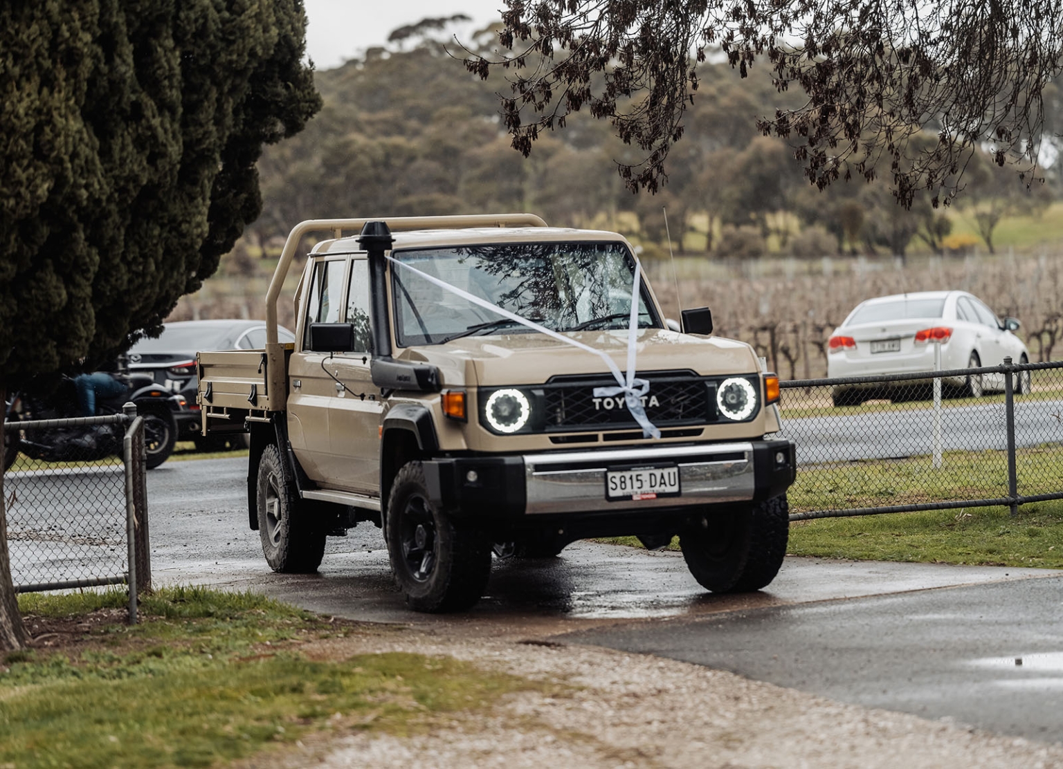 keyneton soldier's memorial hall wedding - lara & simon 3 Beige Toyota ute decorated with white wedding ribbon on a wet driveway at Keyneton Soldier's Memorial Hall.