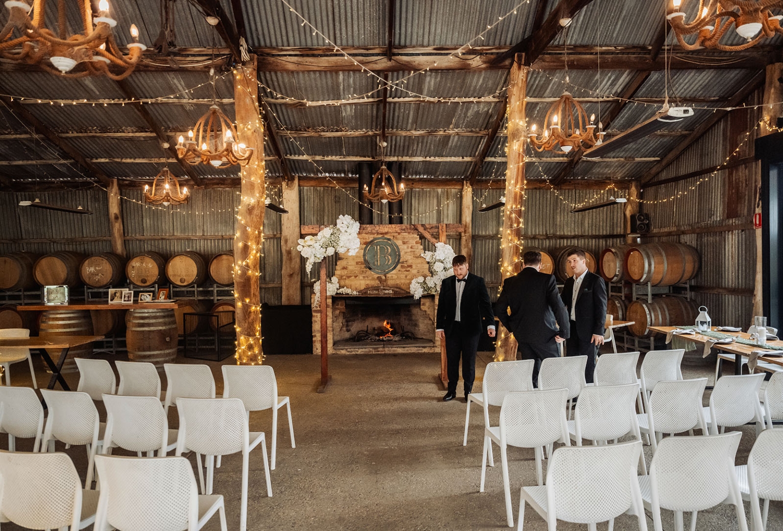 Rustic indoor wedding ceremony space with white chairs, floral arbour, wine barrels and rope chandeliers at Barristers Block