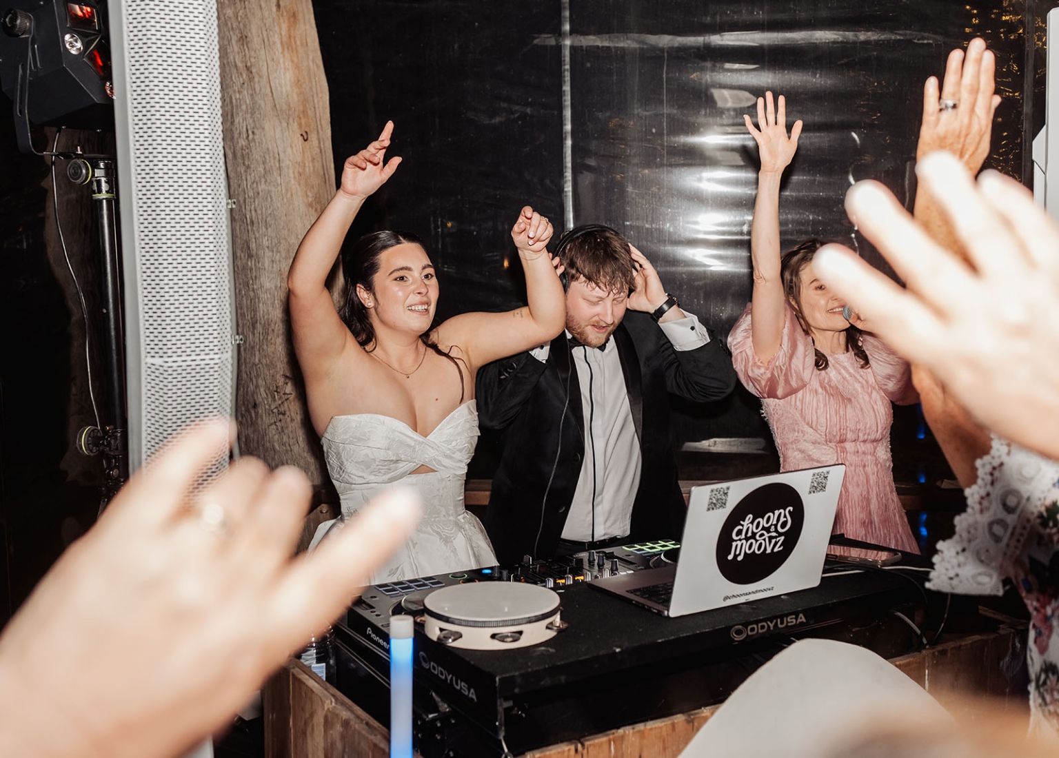 Bride and groom raise their hands beside the DJ booth as wedding guests dance around them at Barristers Block.