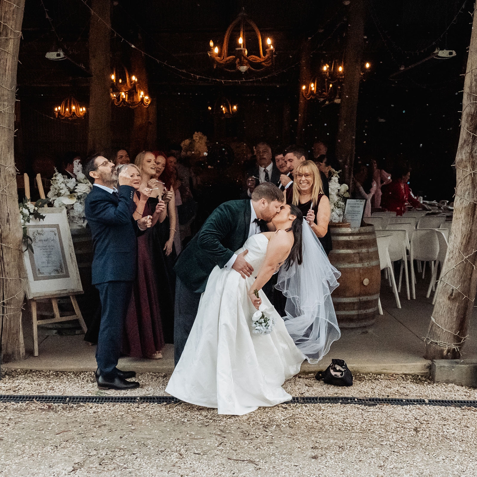 Bride and groom share a kiss as wedding guests blow bubbles beneath chandeliers at Barristers Block