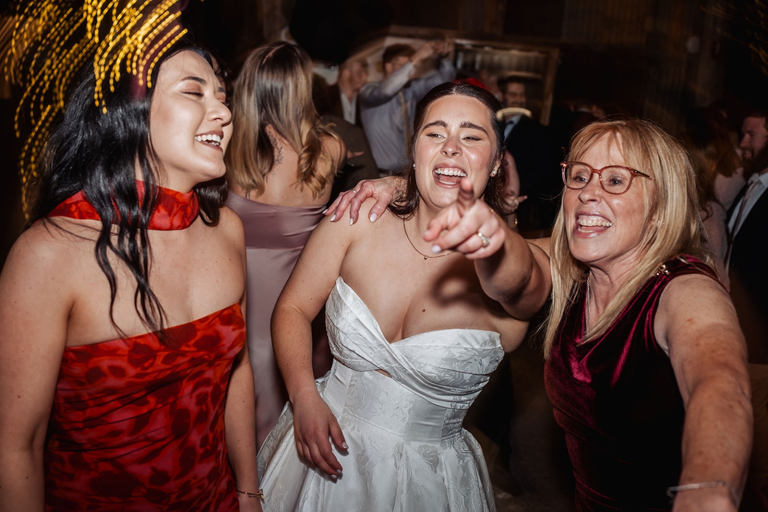 Bride in a white wedding dress laughing and pointing while dancing with guests at the reception
