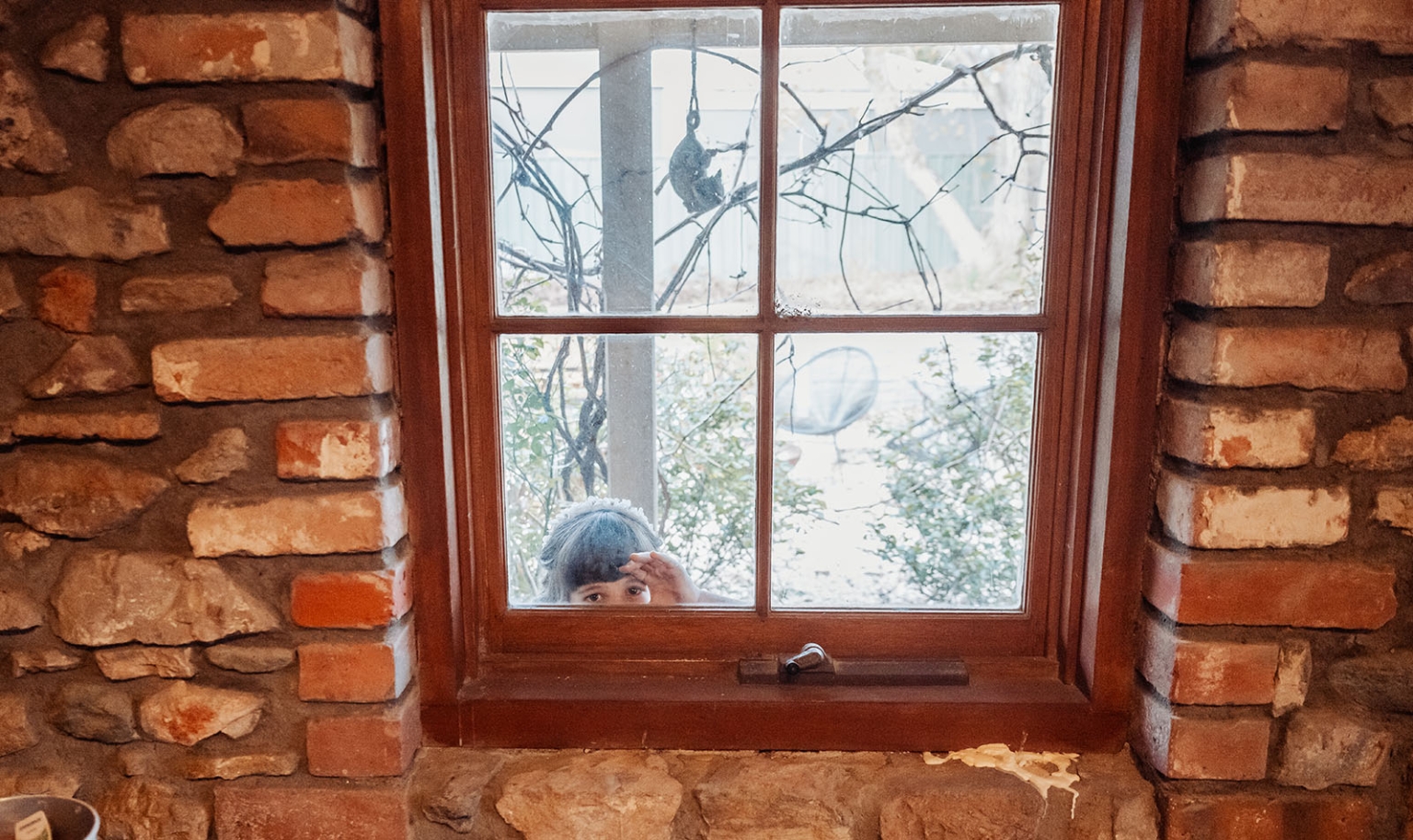 Bride peeking through a timber-framed cottage window set in rustic brick and stone walls