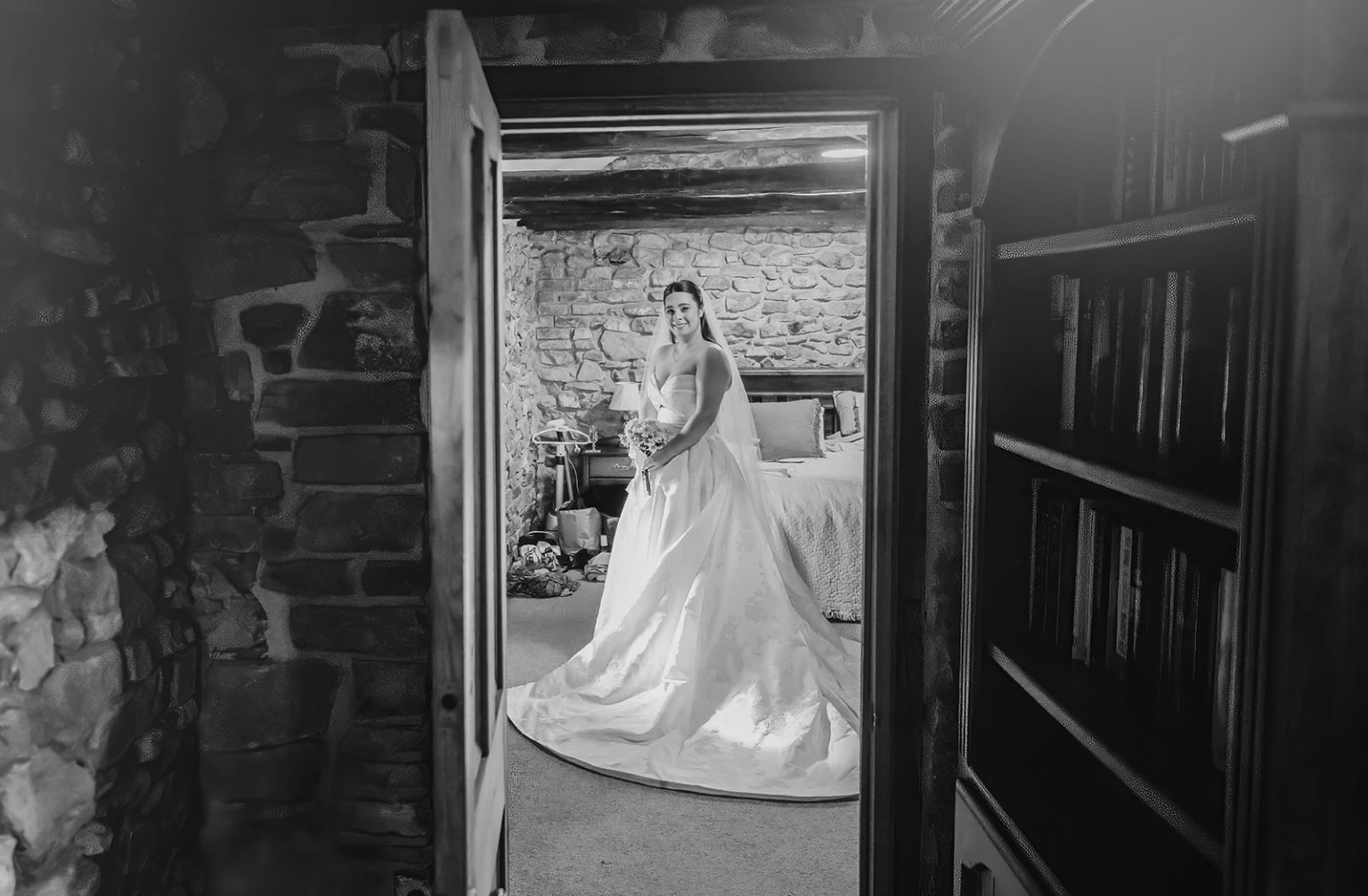 Bride in a wedding gown holding a bouquet in a rustic stone cottage bedroom