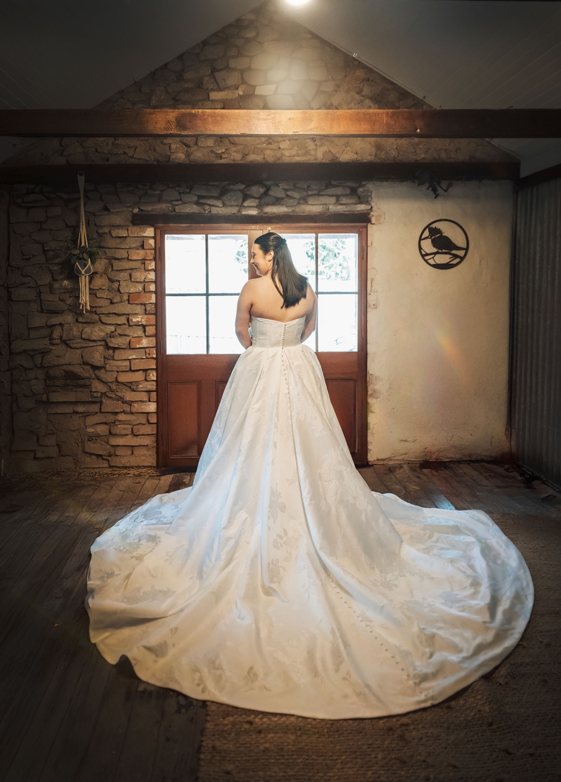 Bride in a strapless white wedding gown standing before a timber-framed window in a rustic stone cottage