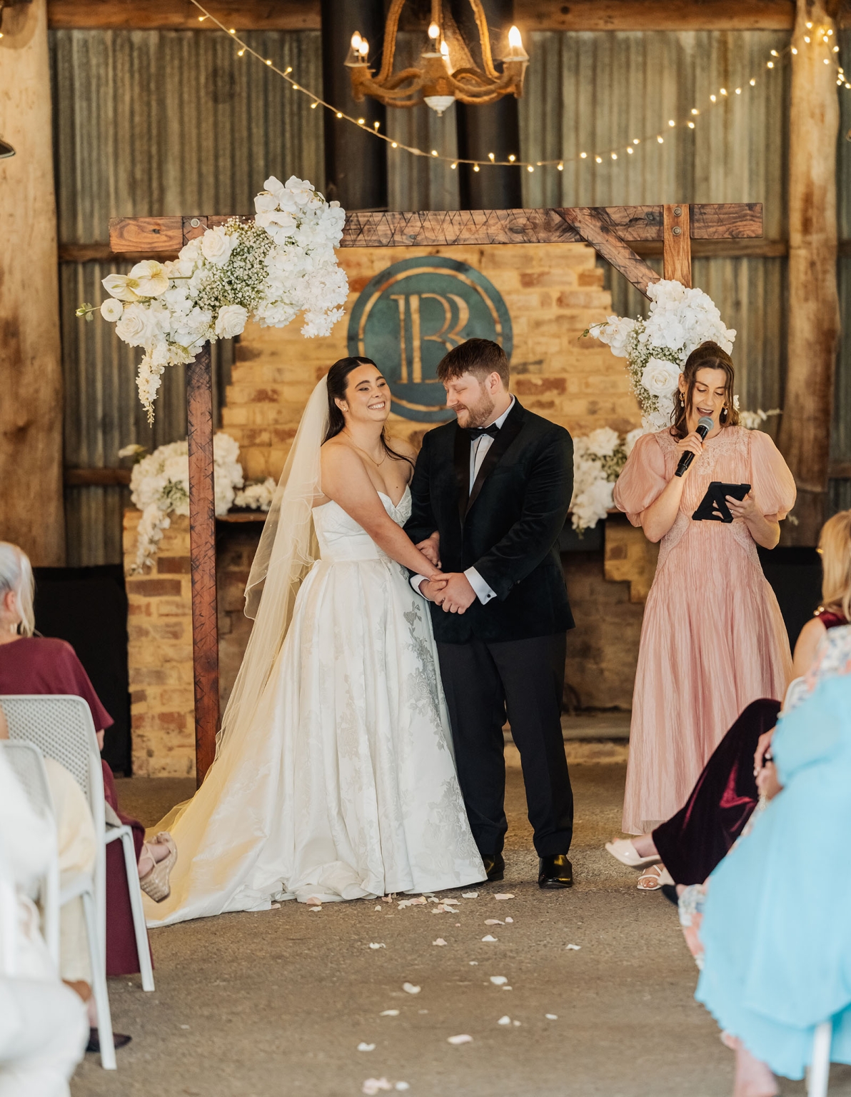 Carley and Corey holding hands beneath a floral timber arbour during their Barristers Block wedding ceremony