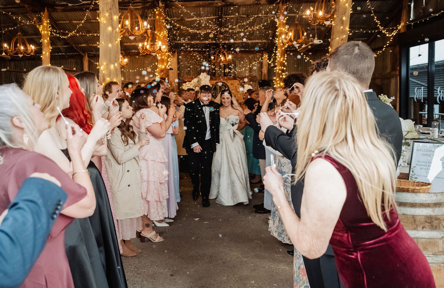 Carley and Corey walk through wedding guests blowing bubbles inside the fairy-lit barn at Barristers Block.