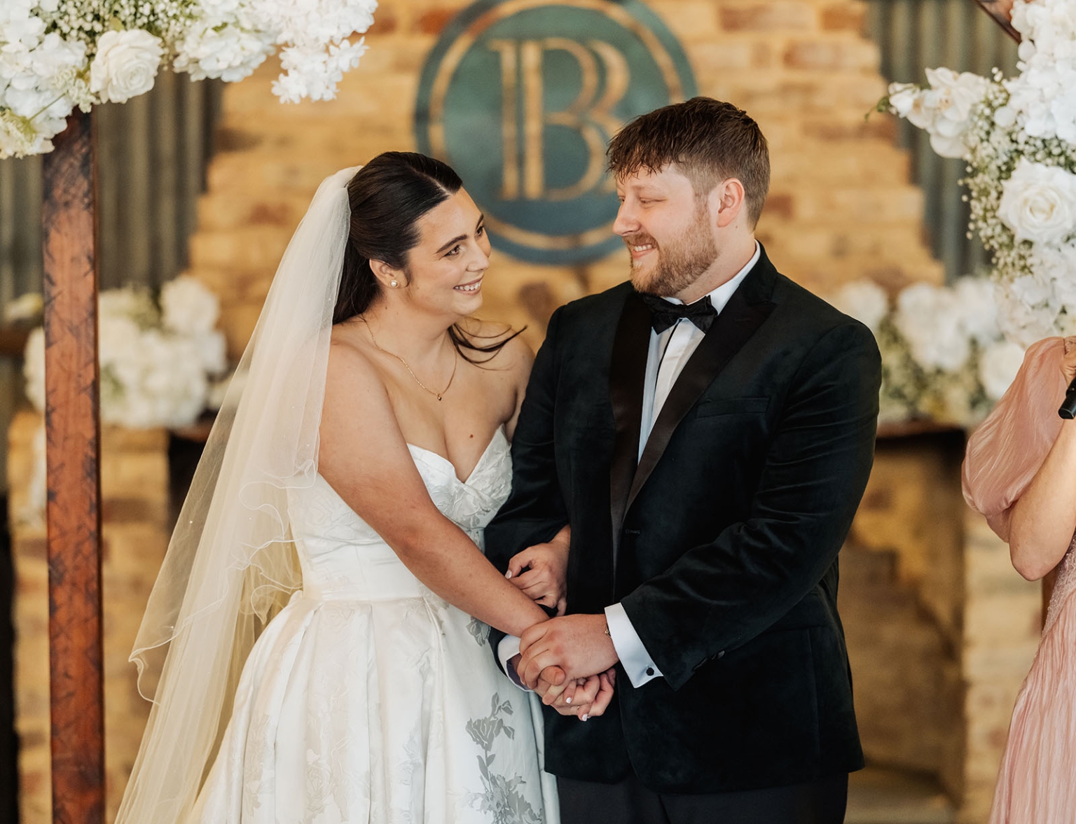 Carley and Corey smiling at each other while holding hands during their wedding ceremony at Barristers Block