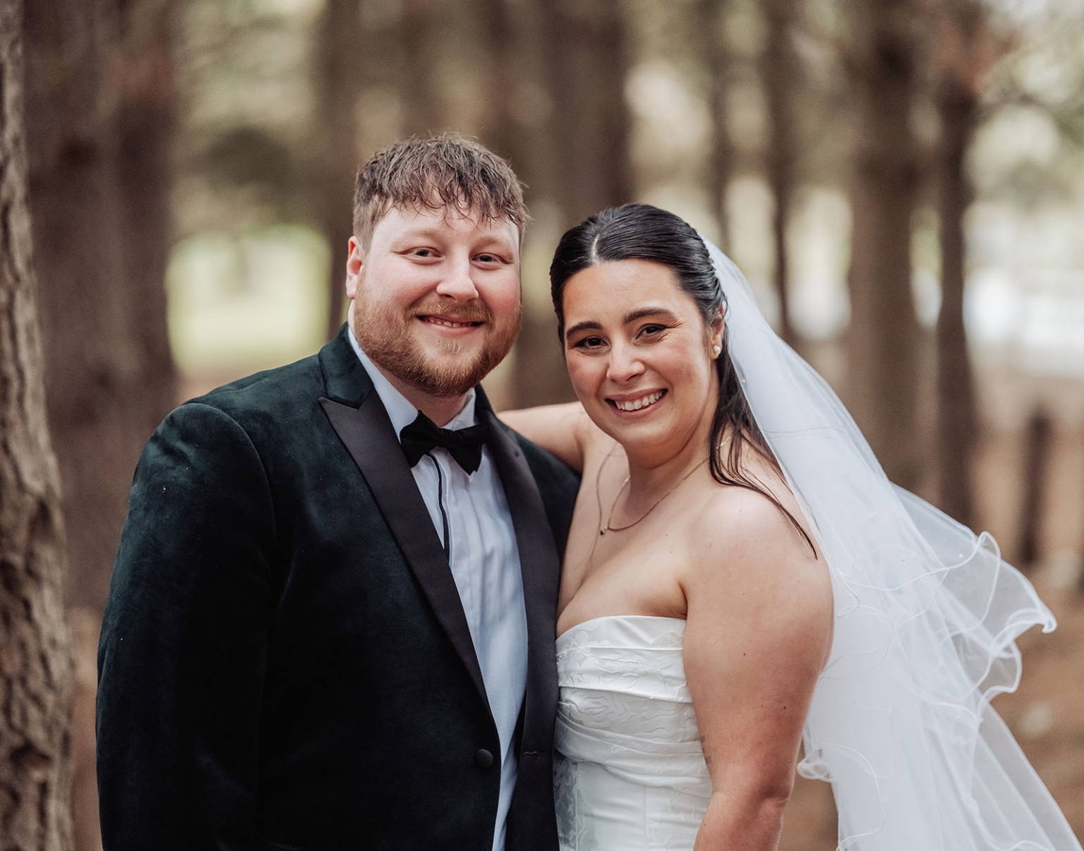Carley and Corey smiling together in wedding attire among tall trees at Barristers Block