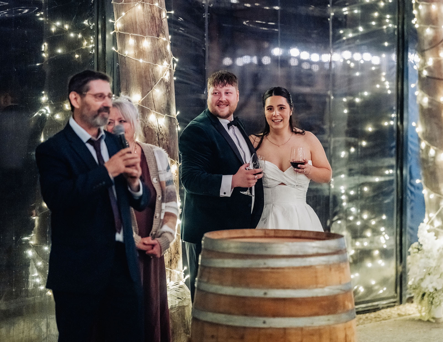 Carley and Corey hold wine glasses beside a wine barrel during their Barristers Block wedding reception as a guest gives a speech.