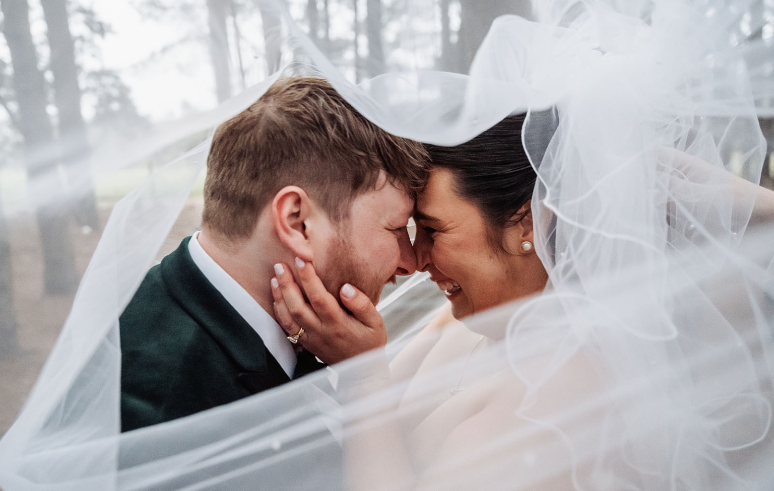 Carley and Corey smiling forehead to forehead beneath the bride’s flowing veil