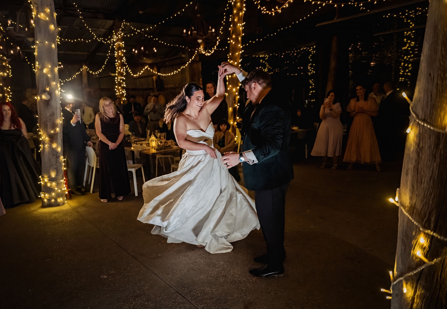 Bride and groom dance beneath warm fairy lights as wedding guests watch at Barristers Block.