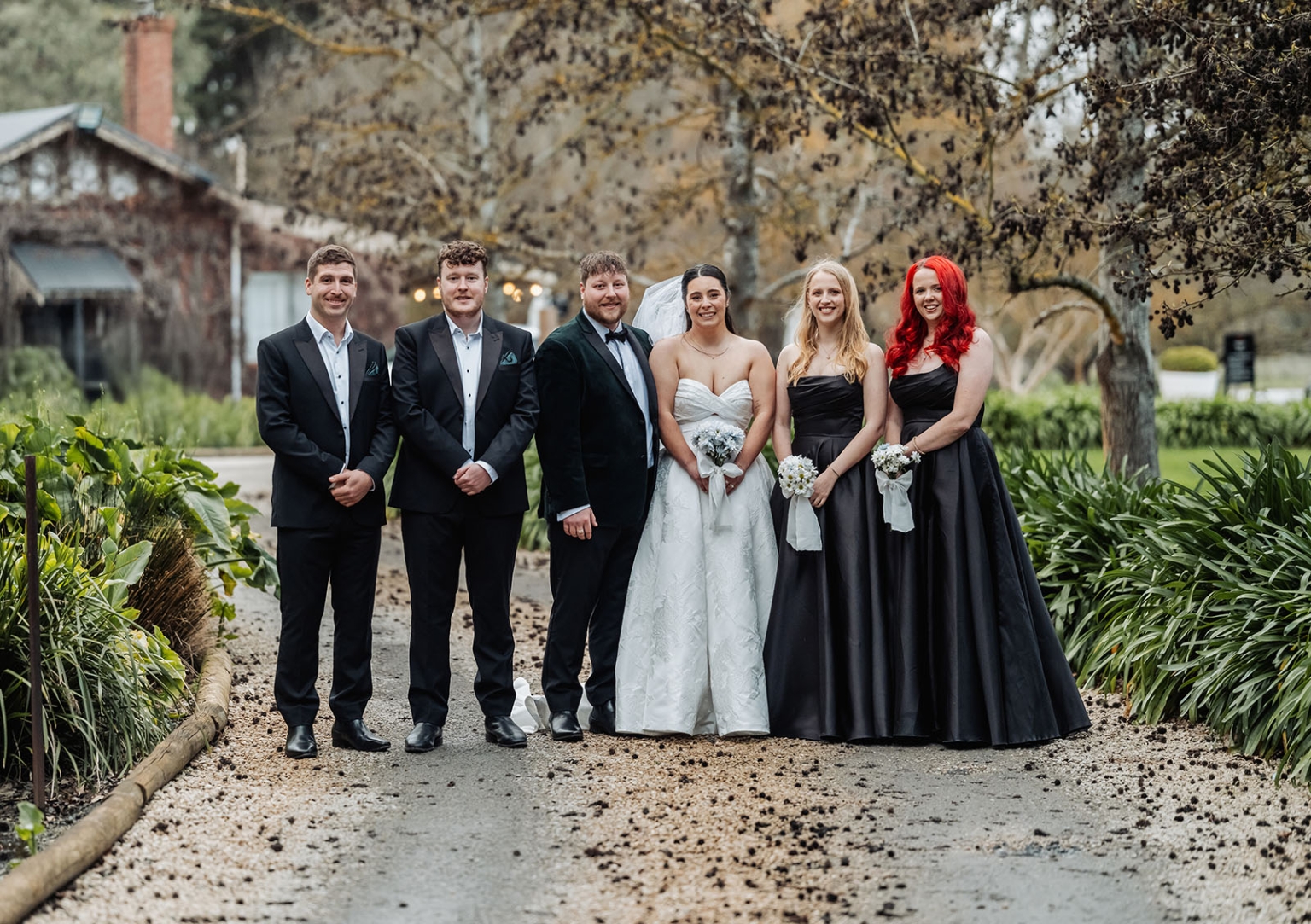 Carley and Corey standing with three wedding party members on a rain-dampened garden path at Barristers Block
