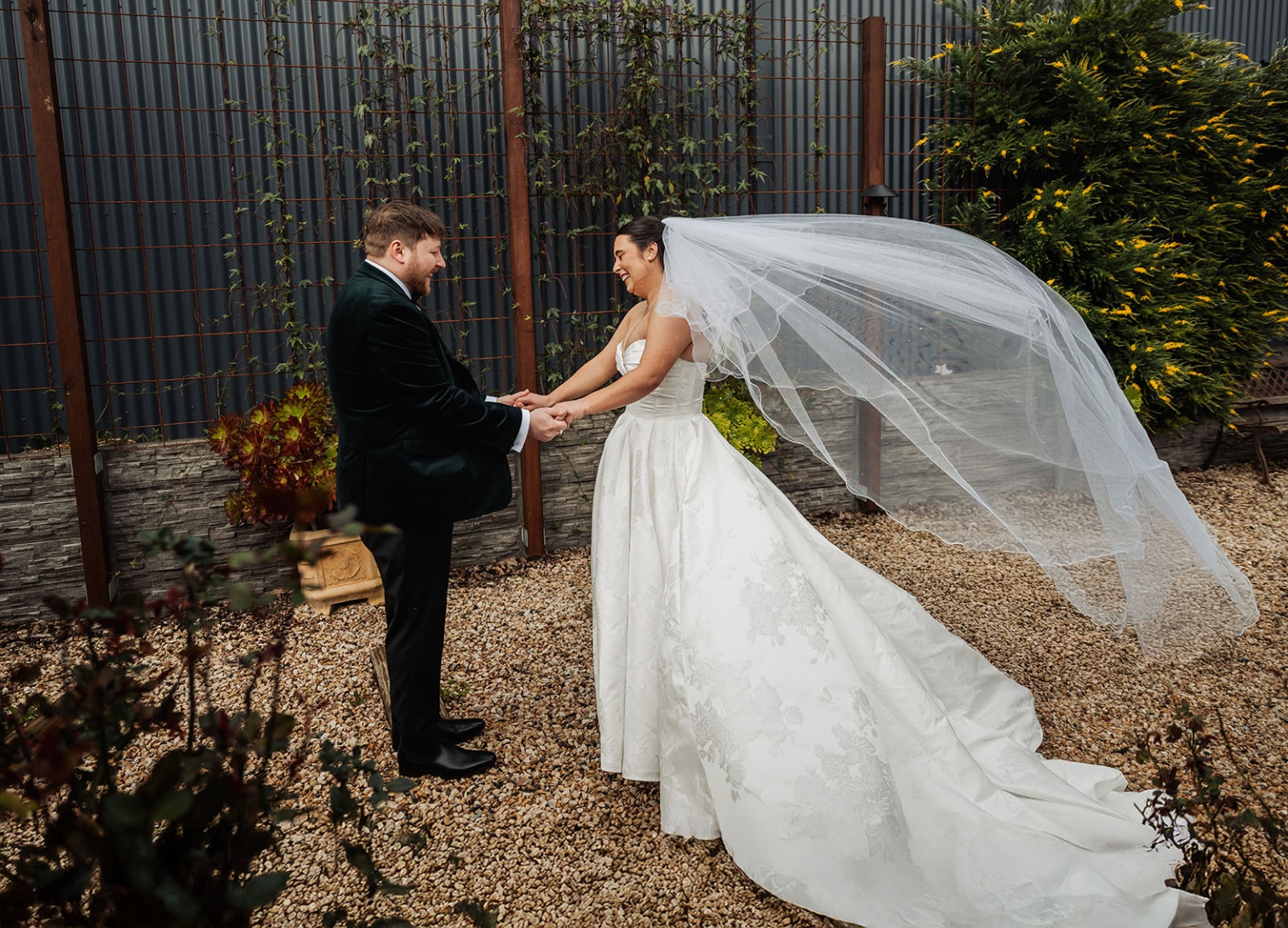Carley and Corey holding hands as her long veil blows behind her at Barristers Block