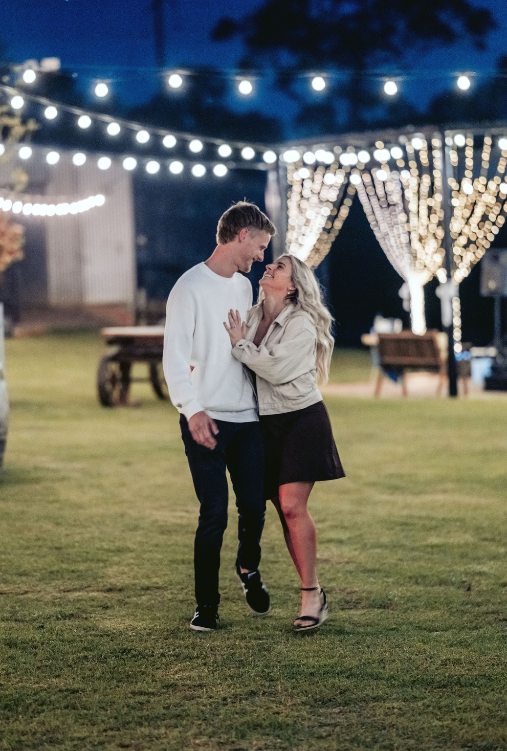 tiny house on the prairie proposal - kyle & bianca 13 Kyle and Bianca smiling together beneath fairy lights on a lawn at night